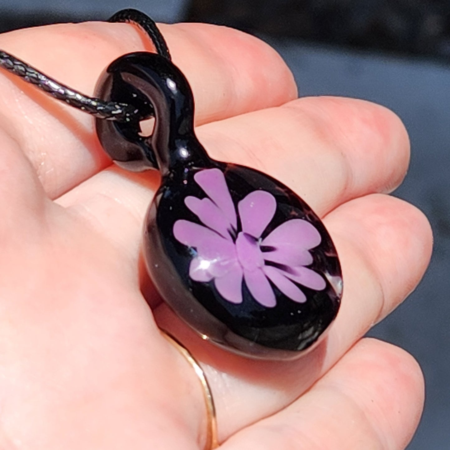 Handmade purple and black glass pendant necklace shown in hand, featuring floral design, perfect for unique gift or personal accessory.