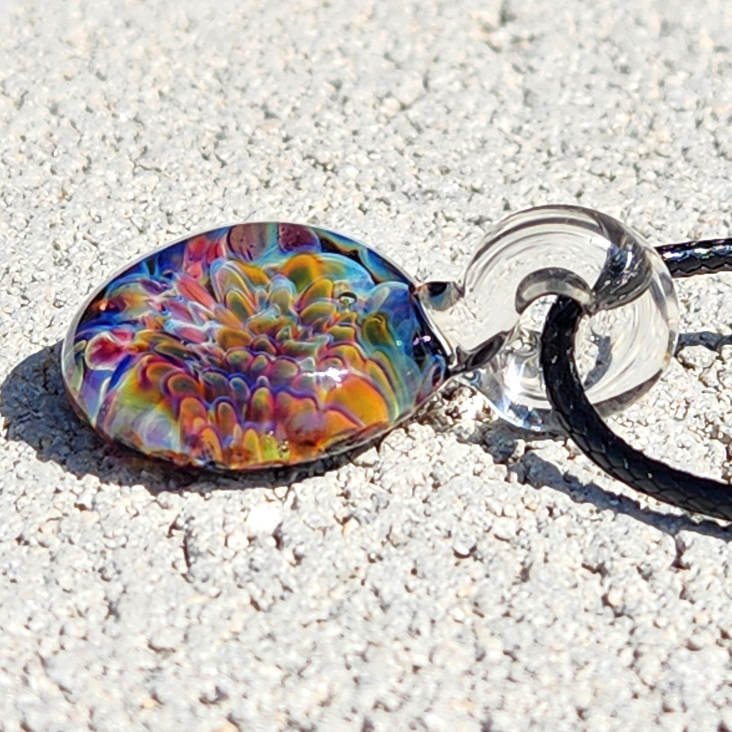 Angled view of Ocean Reef Glass Pendant Necklace with radiant reef design in blue, green, and red, lying on textured stone surface.