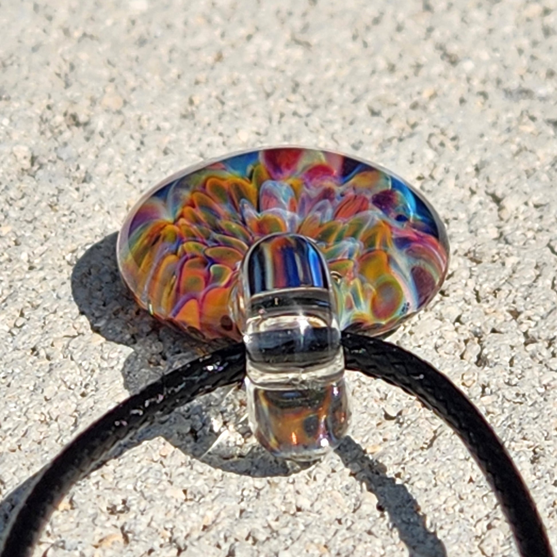 Bottom view of Ocean Reef Glass Pendant showing detailed multicolor reef pattern and clear glass loop with black cord on stone surface.