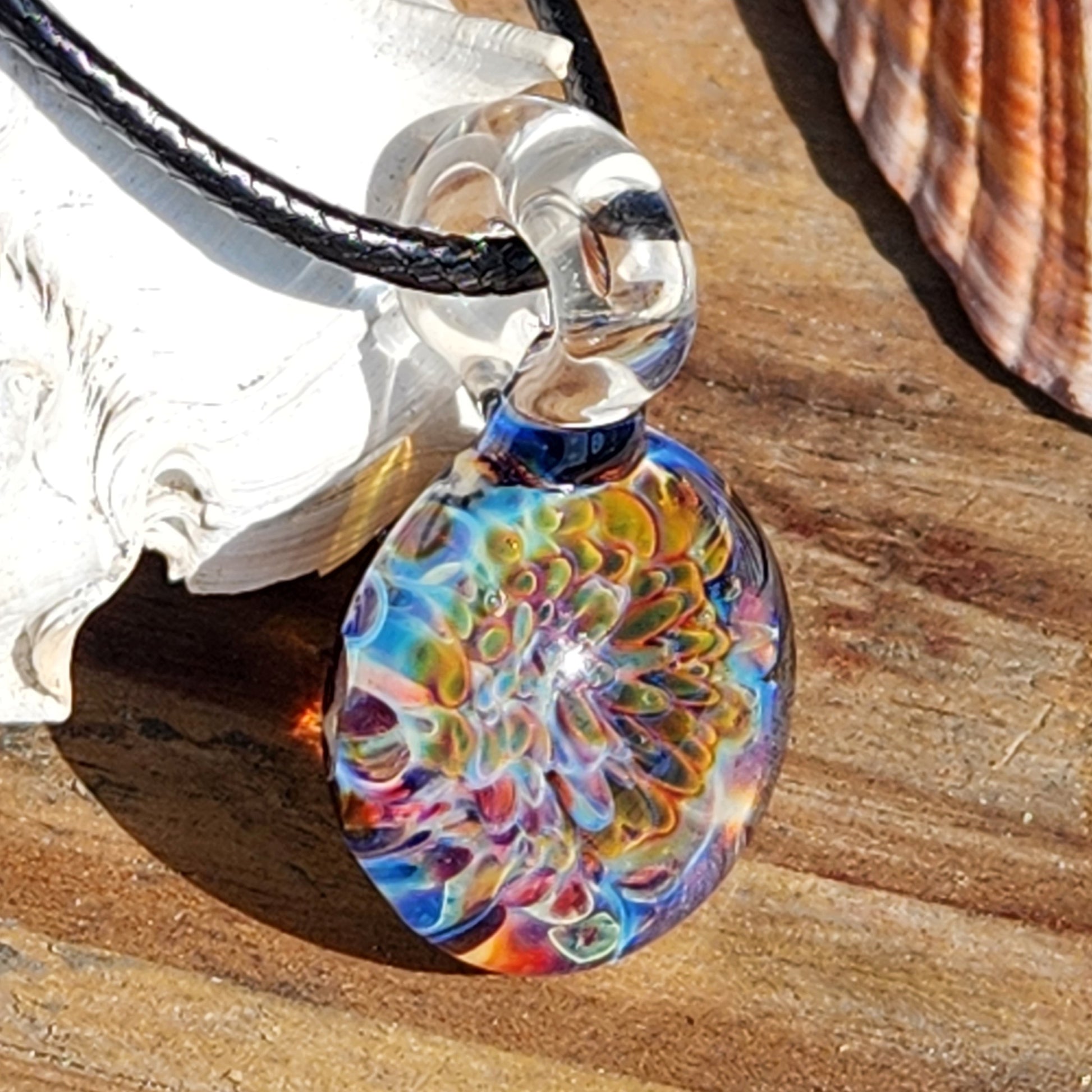 Ocean Reef Glass Pendant Necklace resting on wood with seashell, highlighting handmade multicolor reef pattern and clear glass loop.