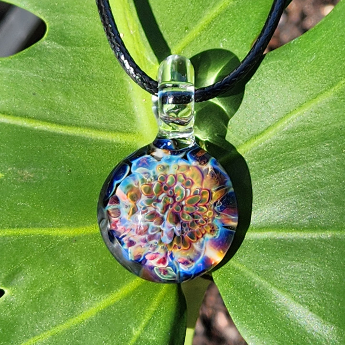 Ocean Reef Glass Pendant Necklace displayed on green leaf, emphasizing colorful reef-inspired glasswork and clear loop bail.