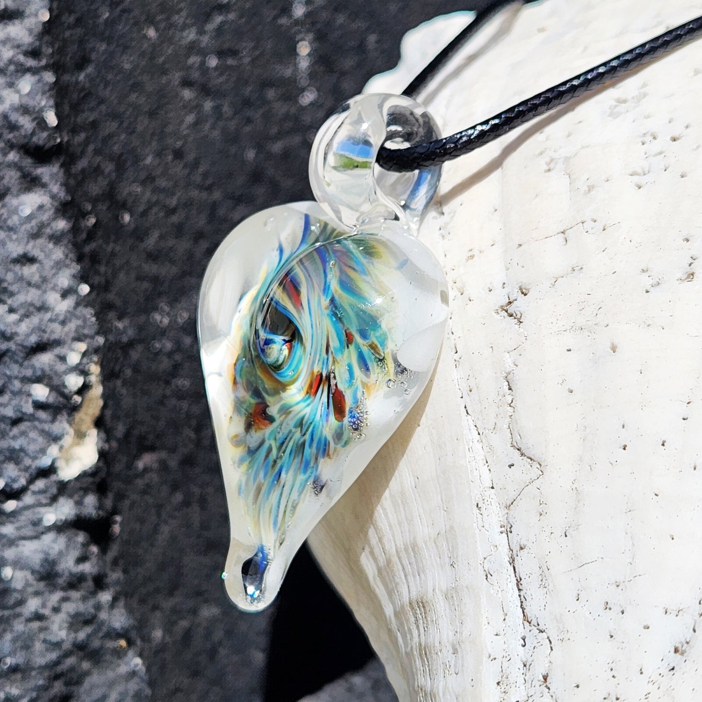 Close-up of handcrafted heart glass pendant with intricate trippy design, featuring multicolor swirls and clear glass loop on black cord.