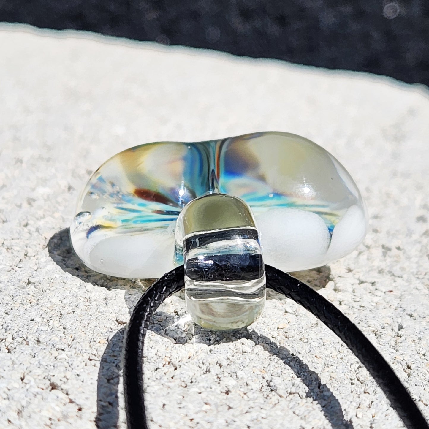 Bottom view of handmade blown glass heart pendant showing clear loop and colorful internal swirls, placed on a light stone surface.