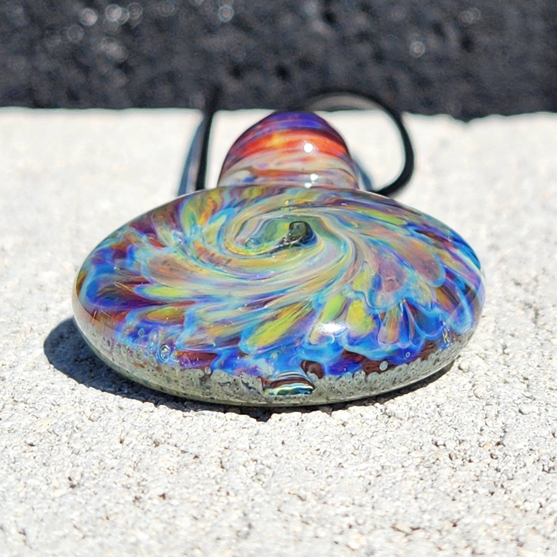 Bottom view of handmade glass pendant with colorful spiral and smooth finish, red loop detail visible on necklace cord.