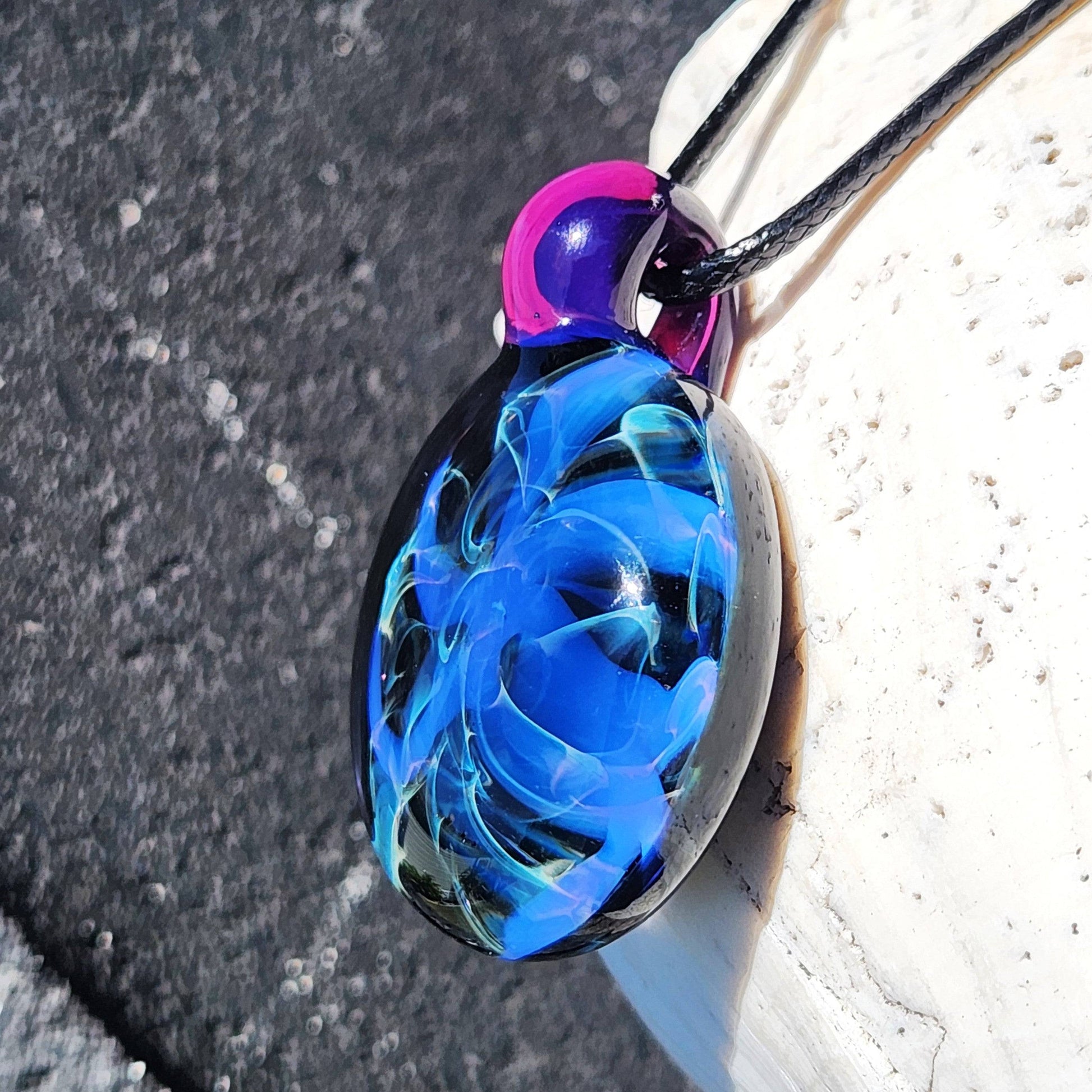 Angled view of Handmade Blue Swirl Glass Pendant Necklace with swirling blue patterns and translucent purple loop.