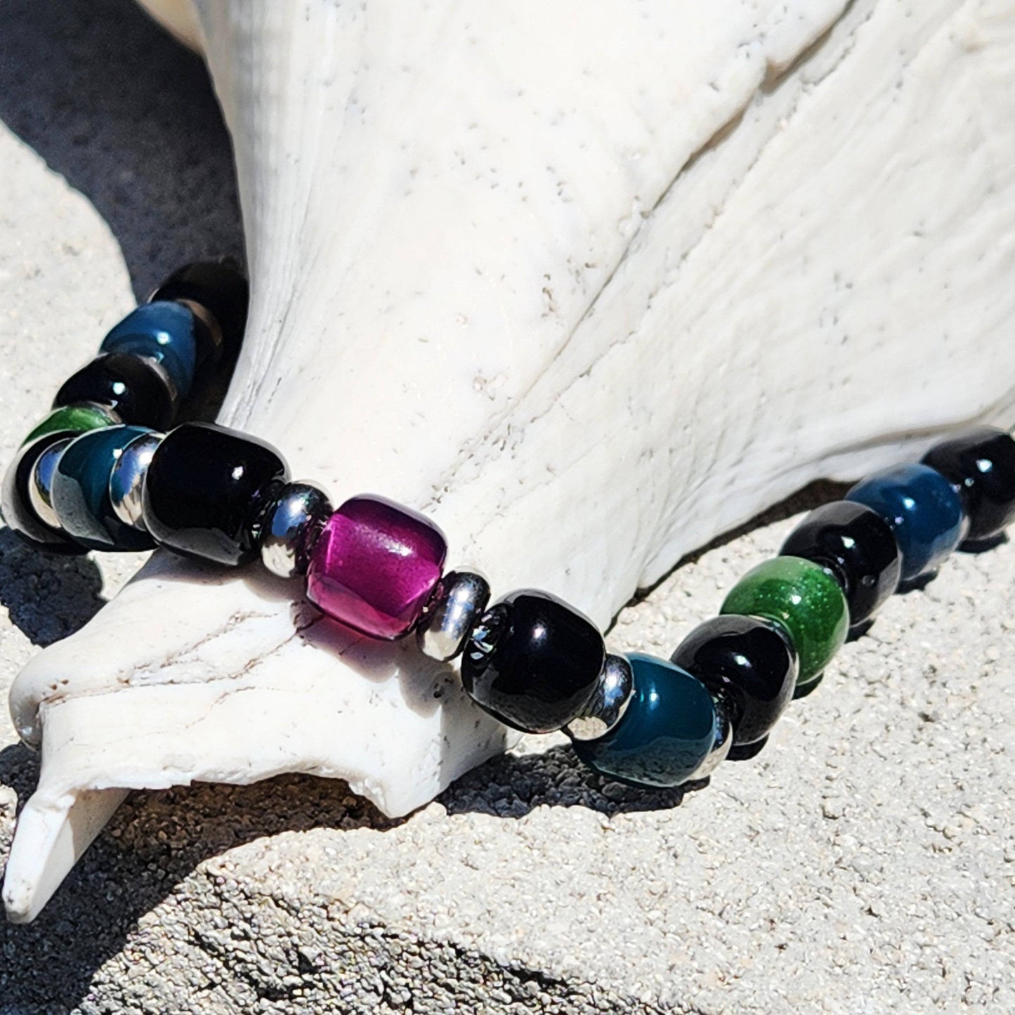 Handmade Boho Glass Beaded Bracelet resting on a seashell, showcasing vibrant purple, green, and blue beads with silver accents.