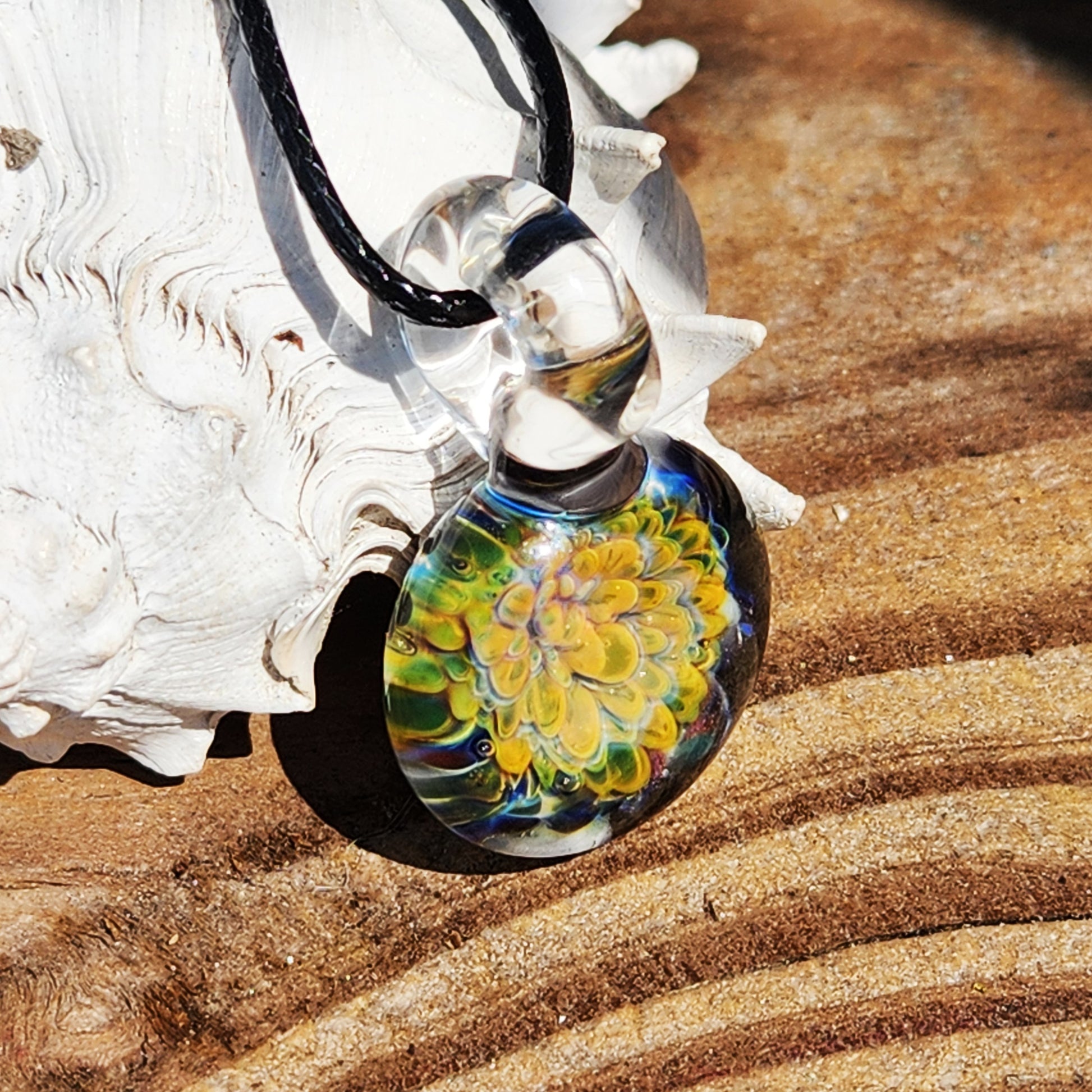 Handmade blown glass pendant with multicolor flower design in green, yellow, and blue tones, suspended on a black cord necklace.