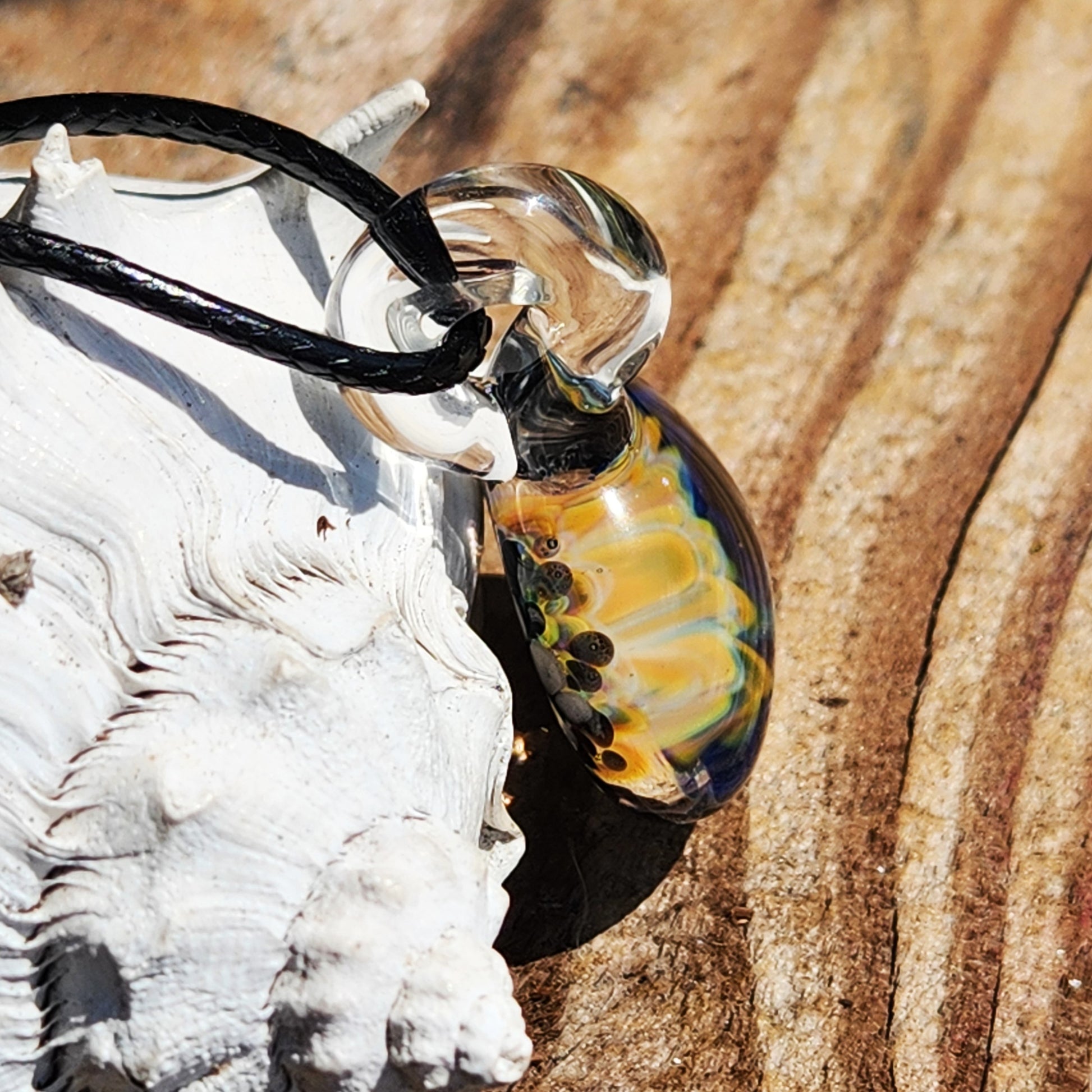 Side view of handmade blown glass pendant with colorful floral core, highlighting its transparent loop and craftsmanship.