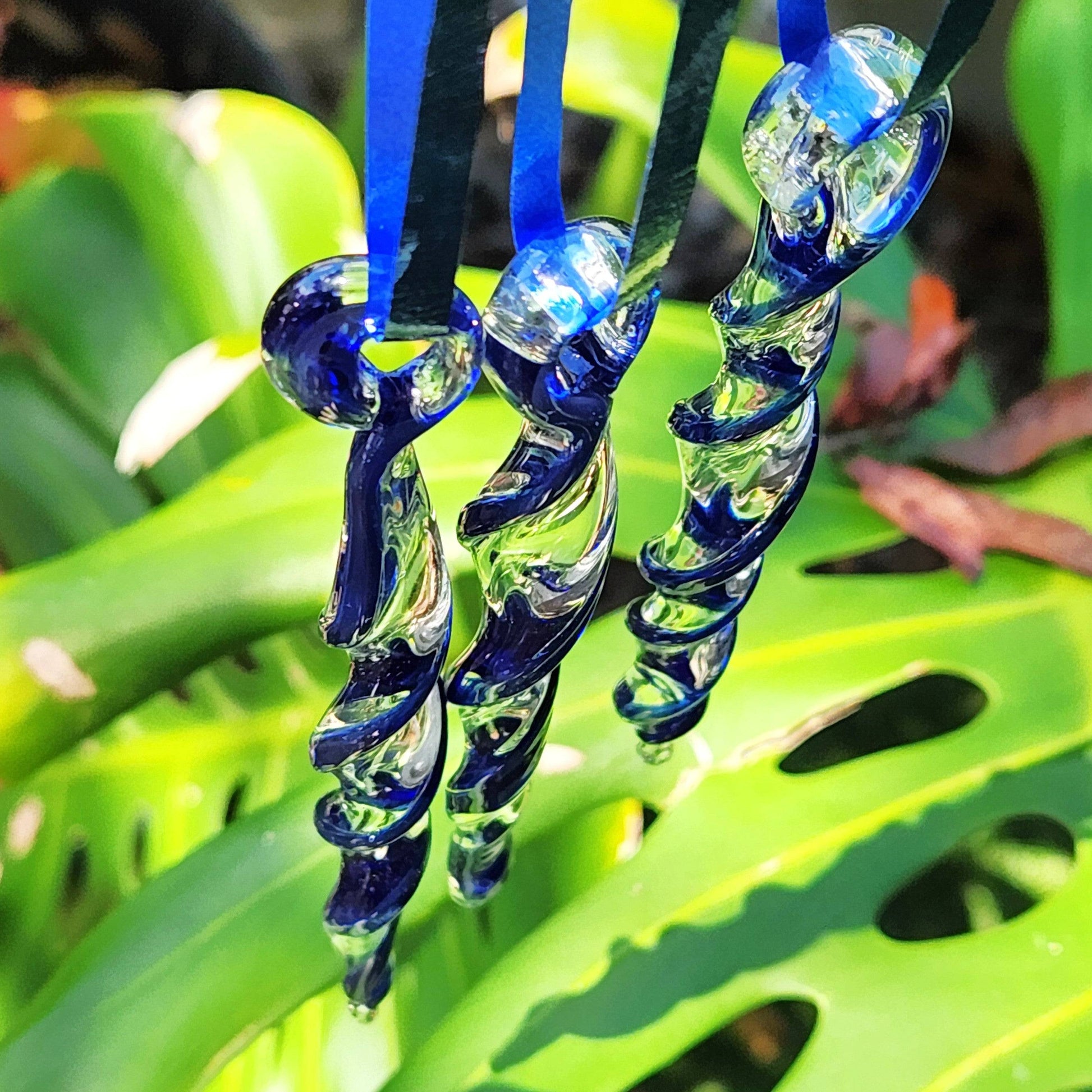 Blue glass Christmas ornaments hanging outdoors against green foliage. Handmade suncatchers add sparkle to garden or holiday décor.