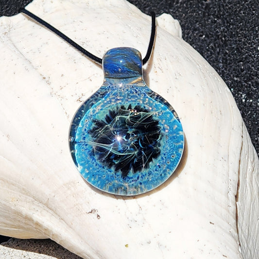 Handmade Pendant Necklace – Winter Scene Borosilicate Glass Pendant with swirling blue and black design on white seashell background.
