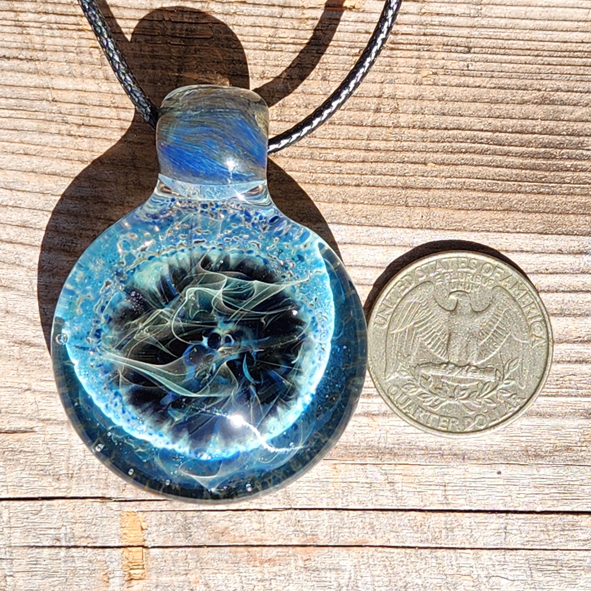 Size comparison of Handmade Pendant Necklace – Winter Scene Borosilicate Glass Pendant next to a US quarter on wood surface.