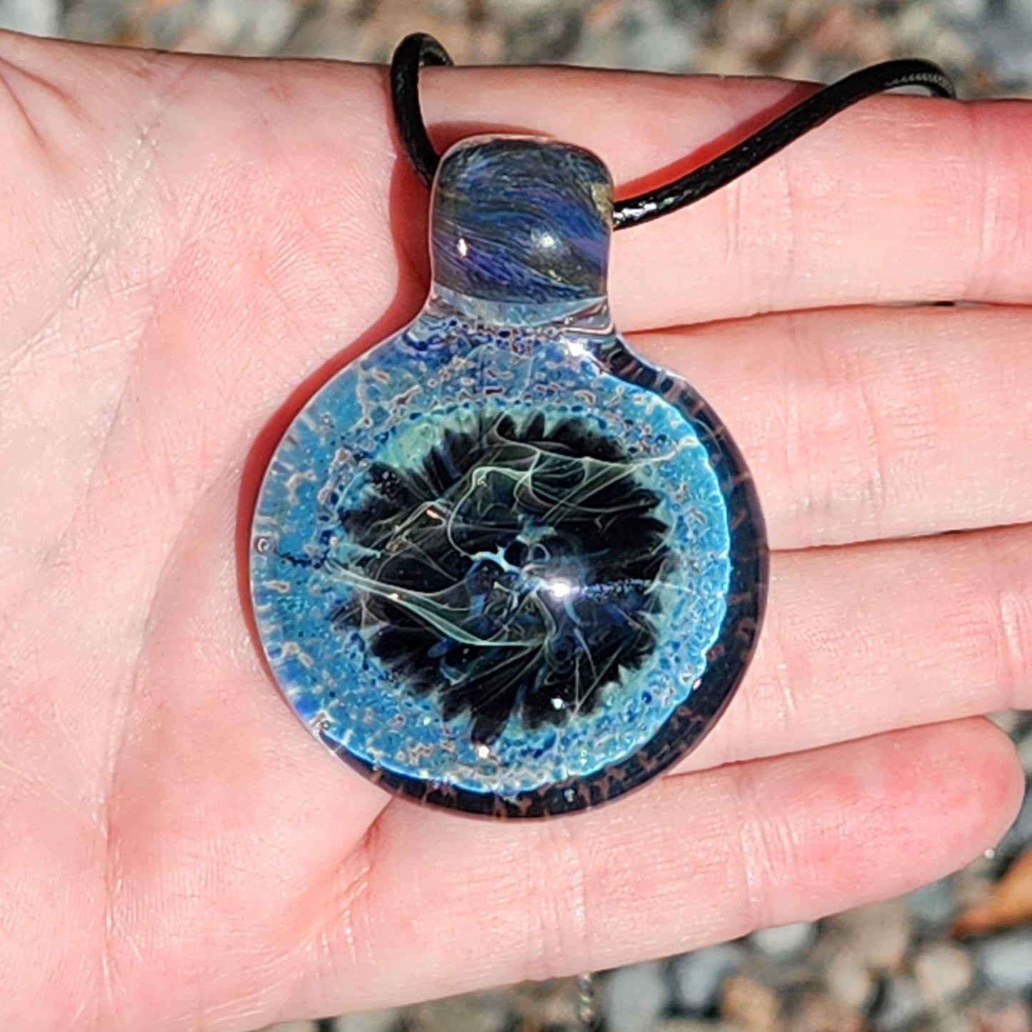 Hand displaying Handmade Pendant Necklace – Winter Scene Borosilicate Glass Pendant with swirling blue and black winter scene.
