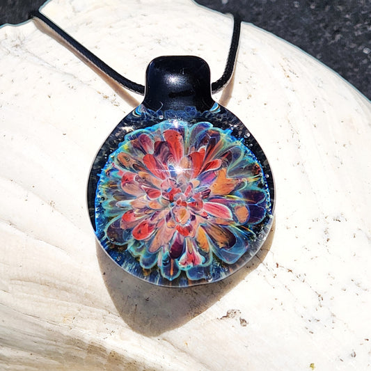 Handmade blown glass pendant necklace with vibrant red, orange, and blue floral design. Unique artisan jewelry gift in borosilicate glass.