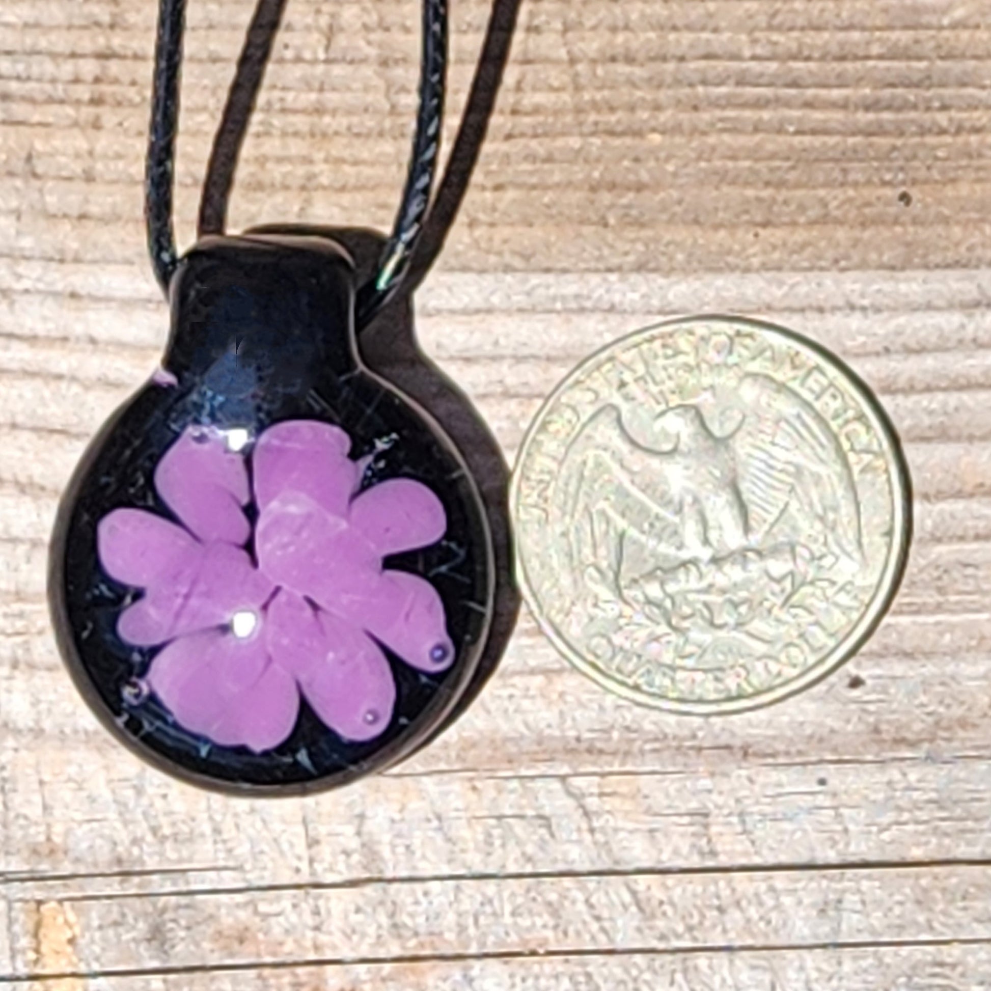Size comparison of small handmade purple glass pendant next to a US quarter, showing its compact and lightweight design.
