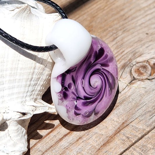 Purple spiral glass pendant necklace with black accents on a white base, displayed on wood with a seashell. Handmade jewelry gift.