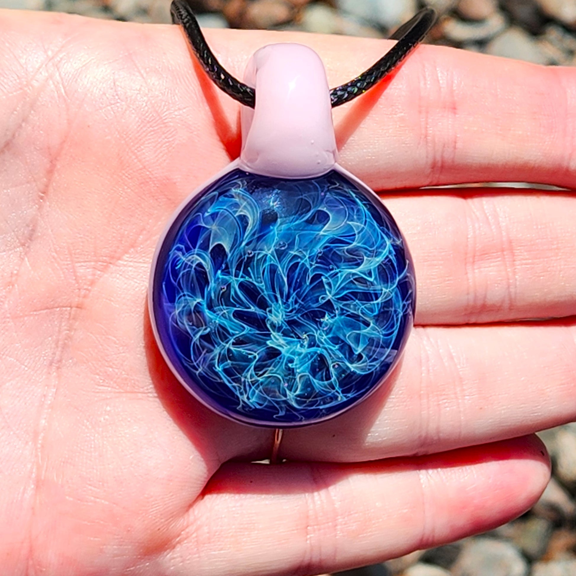 Hand holding small heady glass pendant necklace with pink loop and swirling blue design. Unique handmade jewelry gift for women.