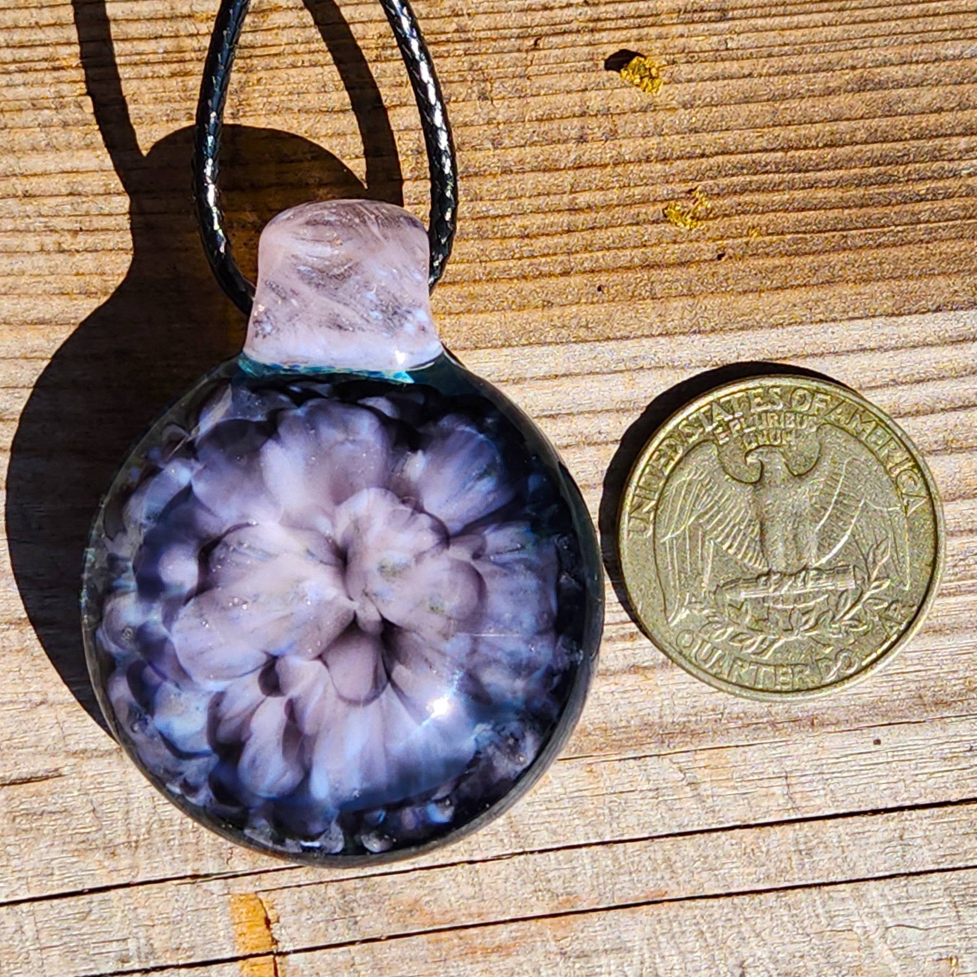 Pink flower pendant necklace next to a US quarter for size comparison, highlighting the compact and wearable design.
