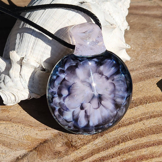 Handmade pink flower pendant necklace with crushed glass design on a black cord, displayed on a seashell over wood surface.