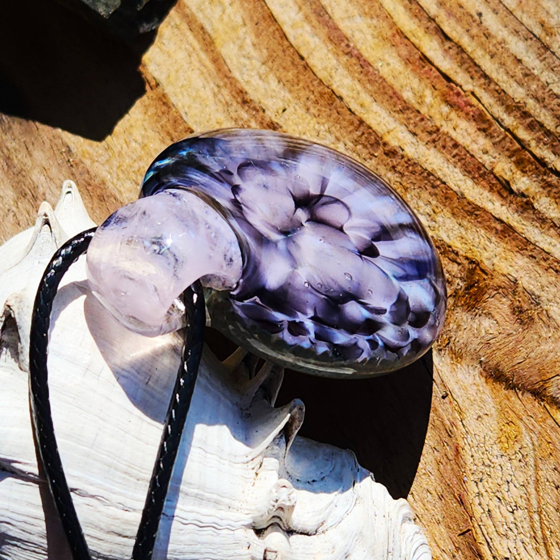 Angled view of pink flower pendant necklace on a shell and wood background, emphasizing the depth of the crushed glass design.