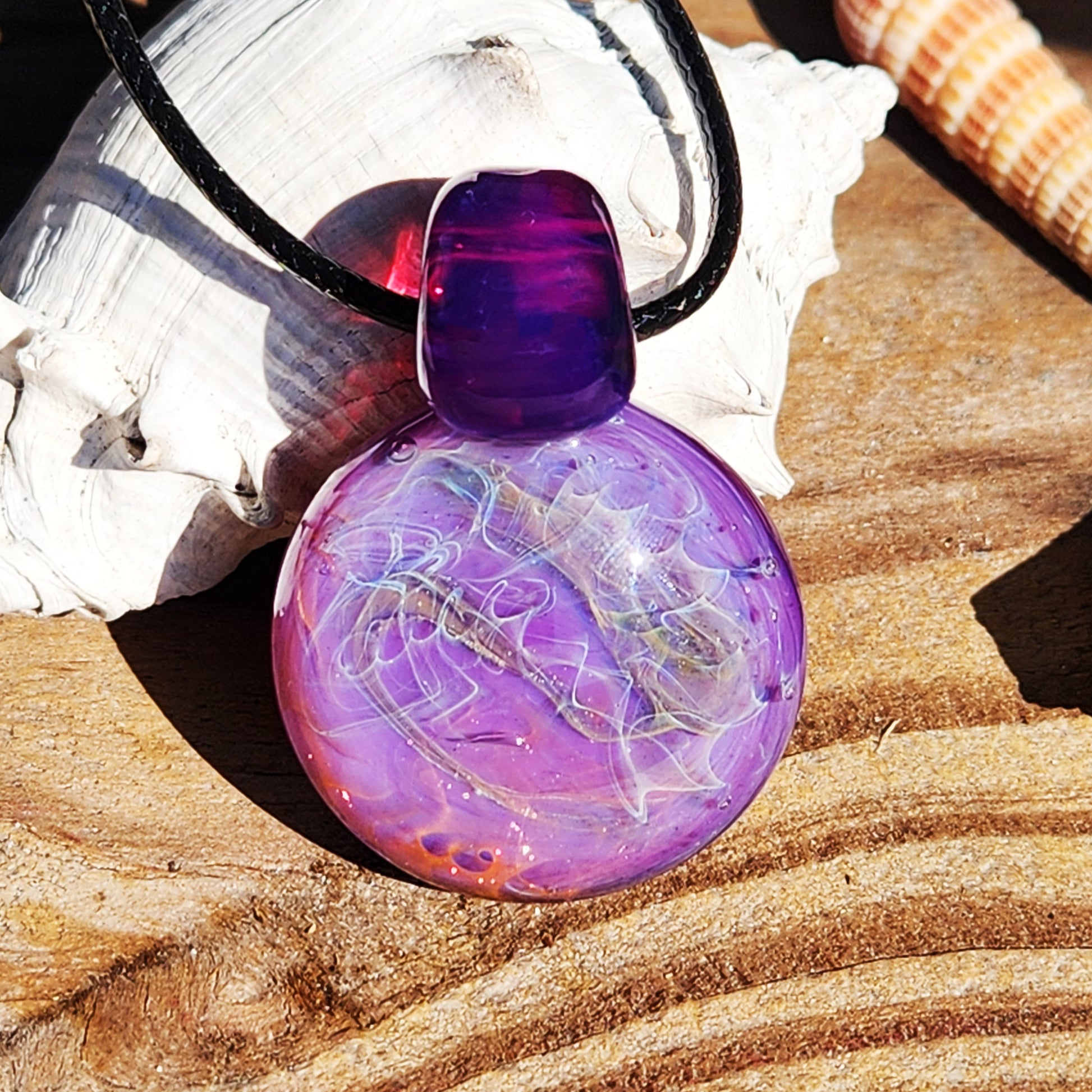 Purple glass pendant necklace with silver and gold fuming, displayed on wood with seashells. Bold artisan jewelry in vivid purple tones.