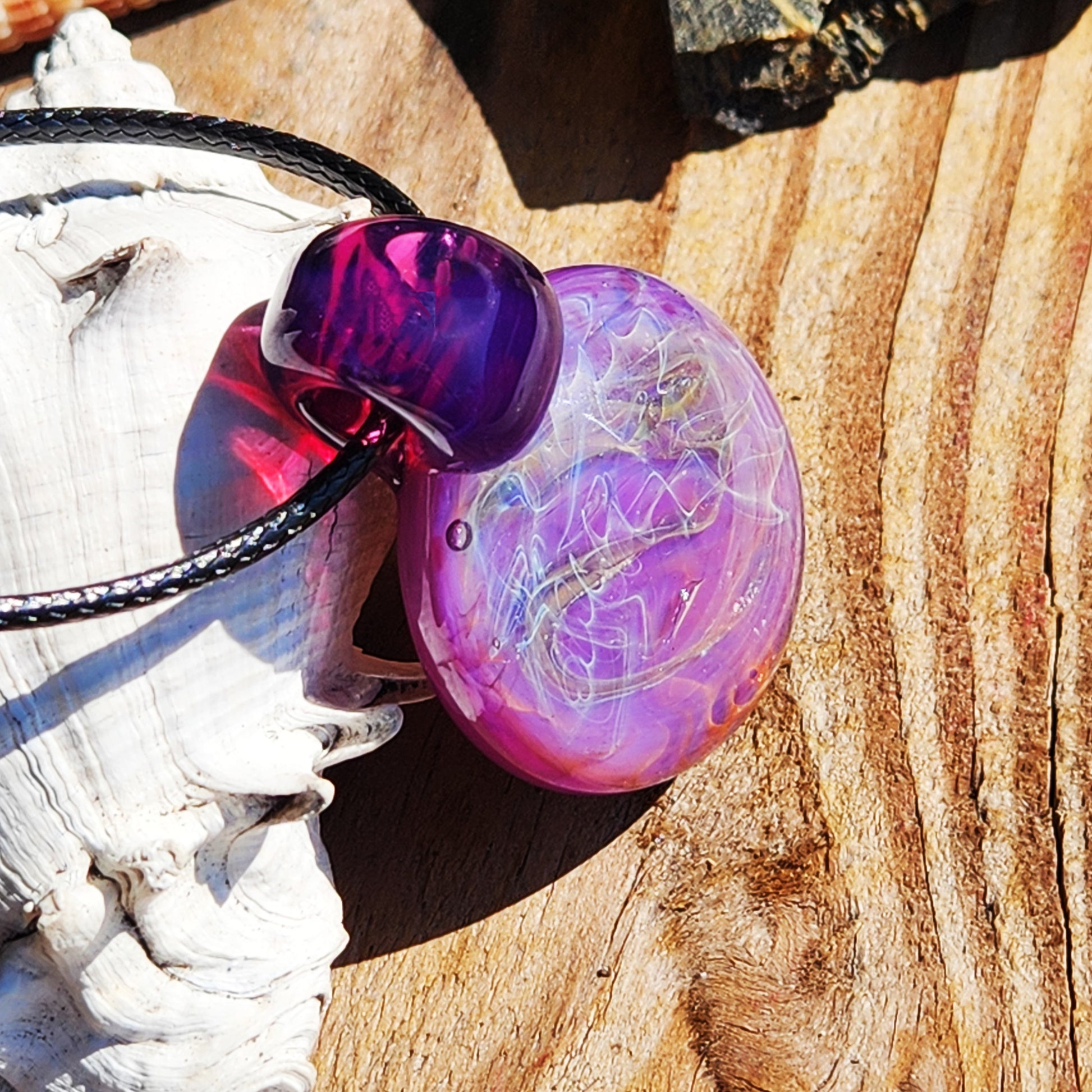 Angled view of purple glass pendant necklace on wood. Features silver and gold fuming with a bold, artistic design.