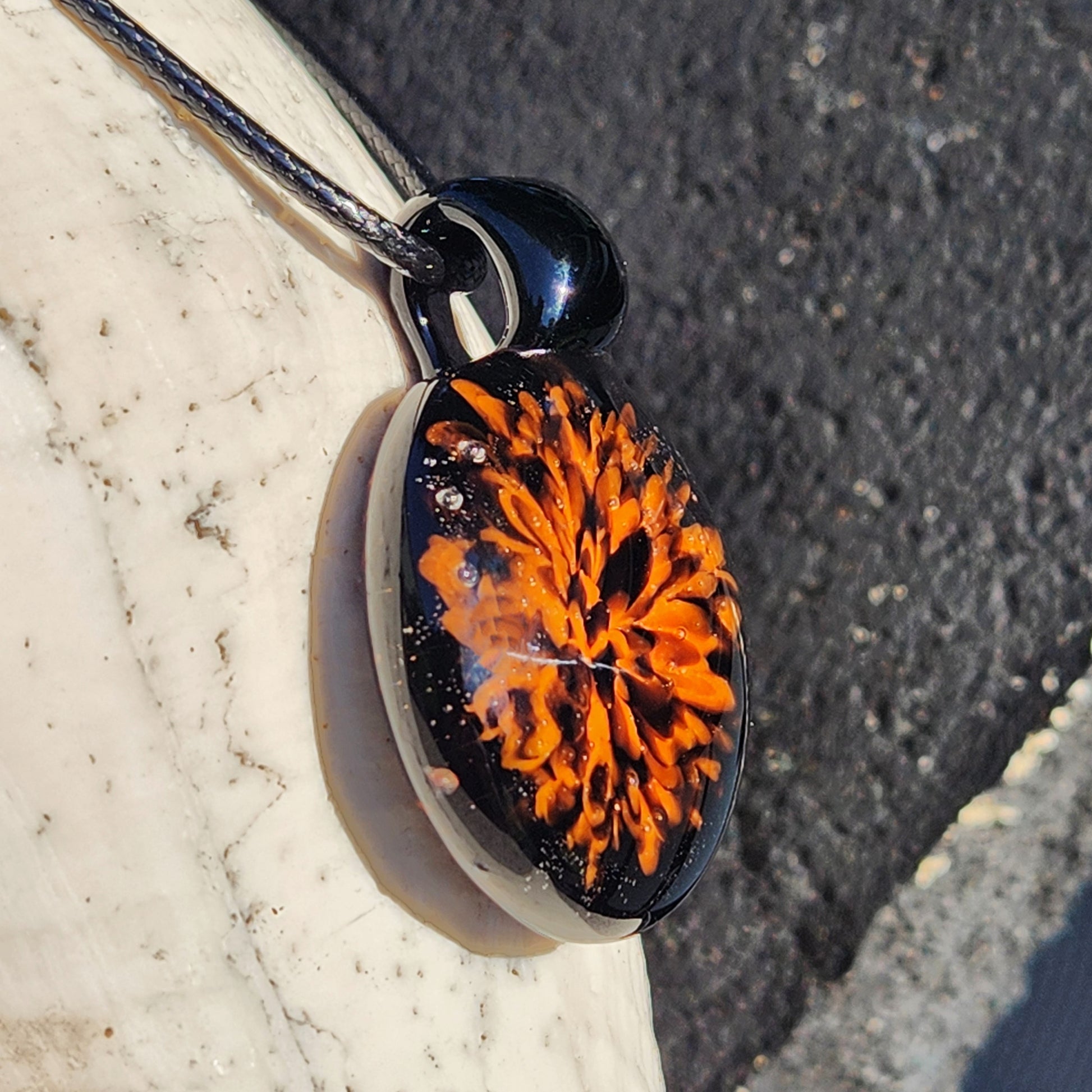 Angled shot of the Fiery Glass Pendant Necklace highlighting the intricate orange bloom and crushed black glass accents. Halloween-themed artisan jewelry.