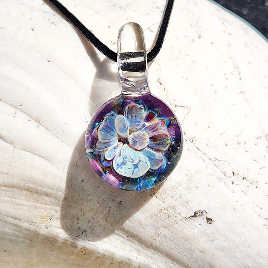 Handmade Borosilicate Glass Pendant with blue and purple bloom on black cord, shown on a white seashell background.