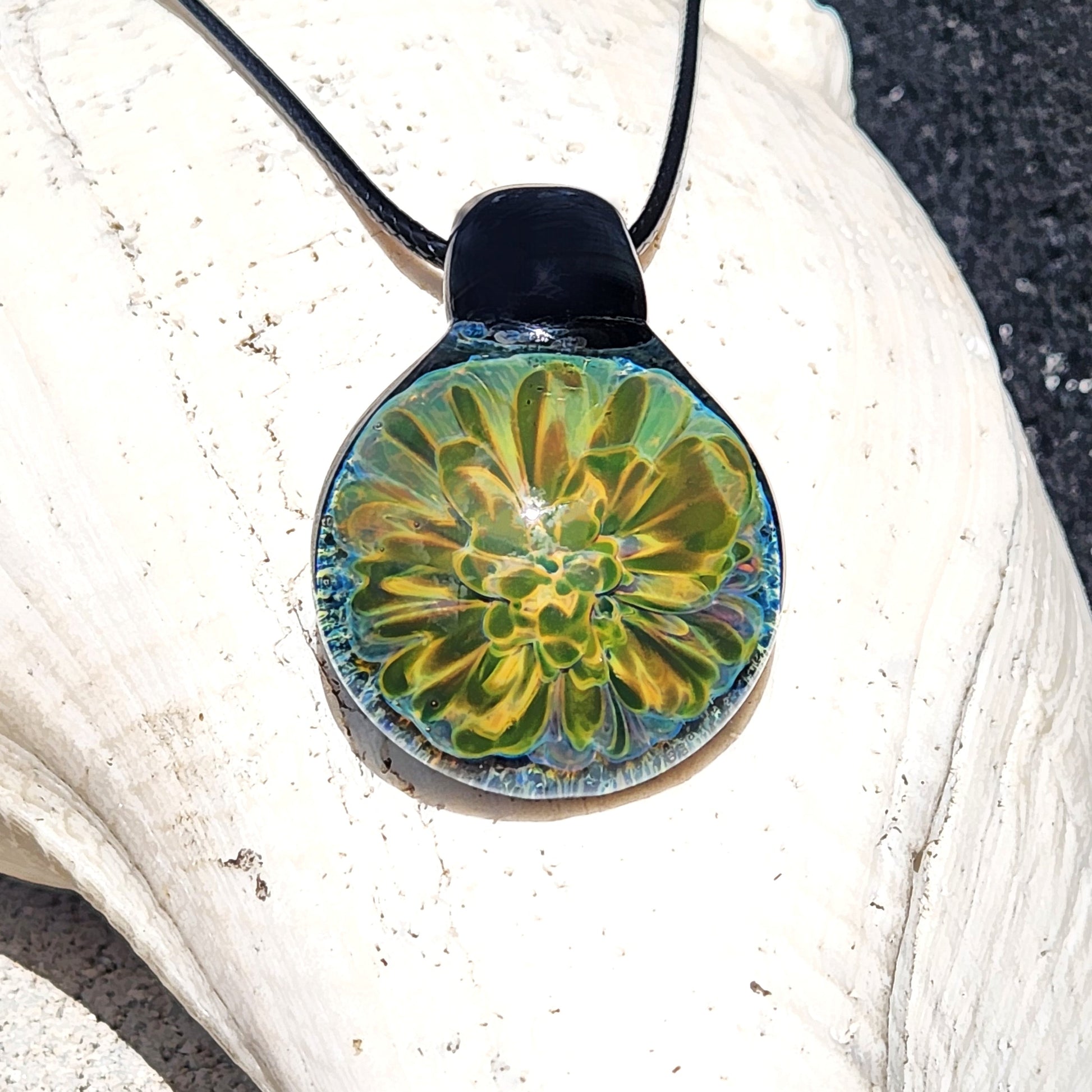 Handmade glass pendant with glowing yellow-green floral design on black cord, displayed on a white seashell. Unique jewelry gift in gift box.