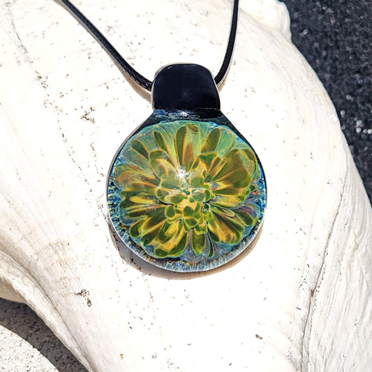 Handmade glass pendant with glowing yellow-green floral design on black cord, displayed on a white seashell. Unique jewelry gift in gift box.