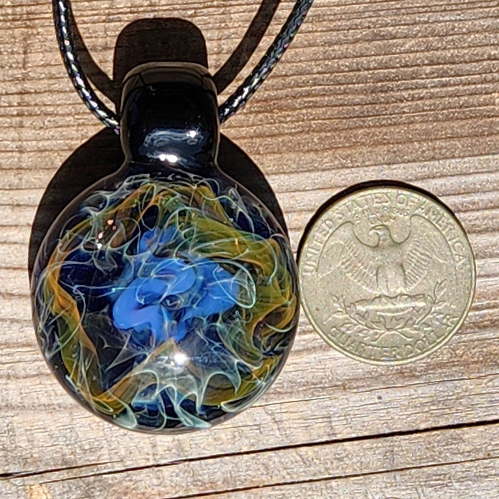 Size comparison of handmade glass pendant with a U.S. quarter, showing detailed gold and blue cosmic swirls on a black background.