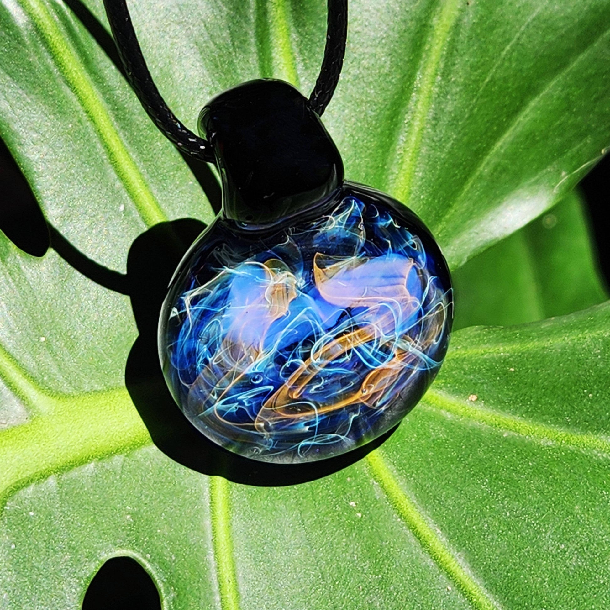 Handmade Glass Pendant – Unique Gold & Silver Fumed Black Necklace featuring vibrant blue, gold, and silver swirls on green leaf.