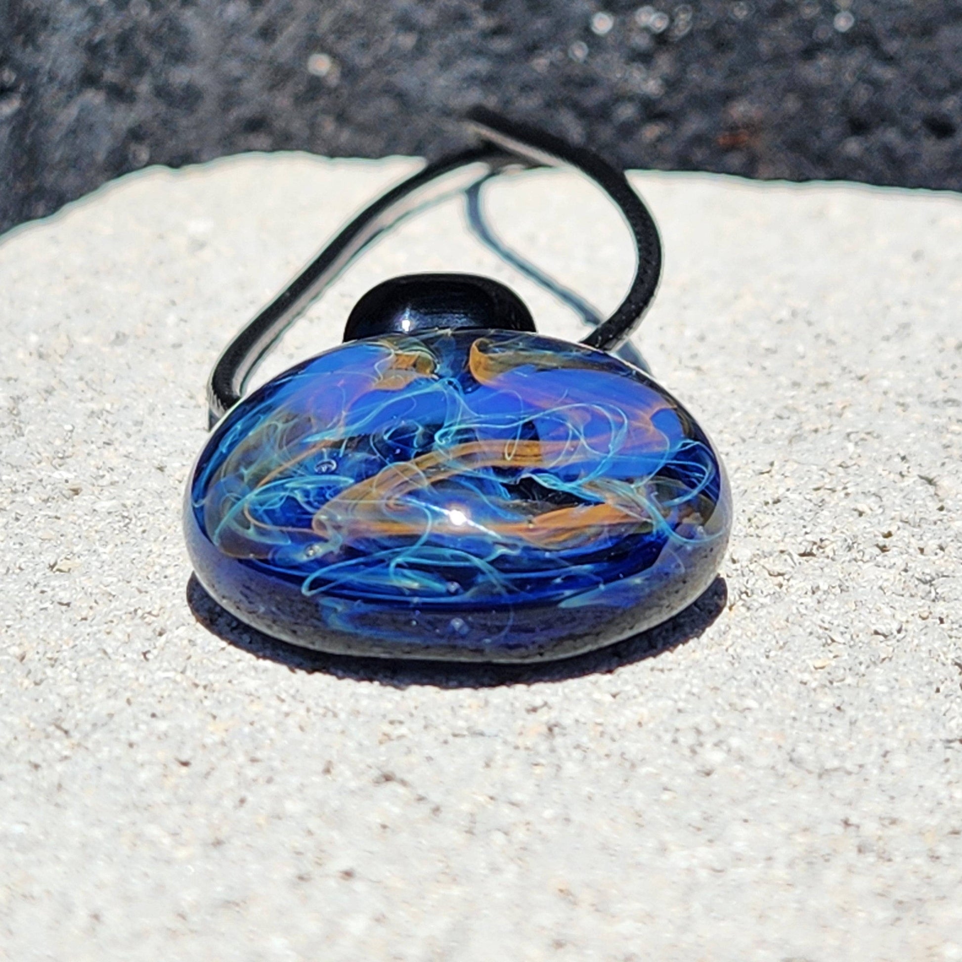 Flat view of Handmade Glass Pendant – Unique Gold & Silver Fumed Black Necklace resting on stone surface with vivid colors.