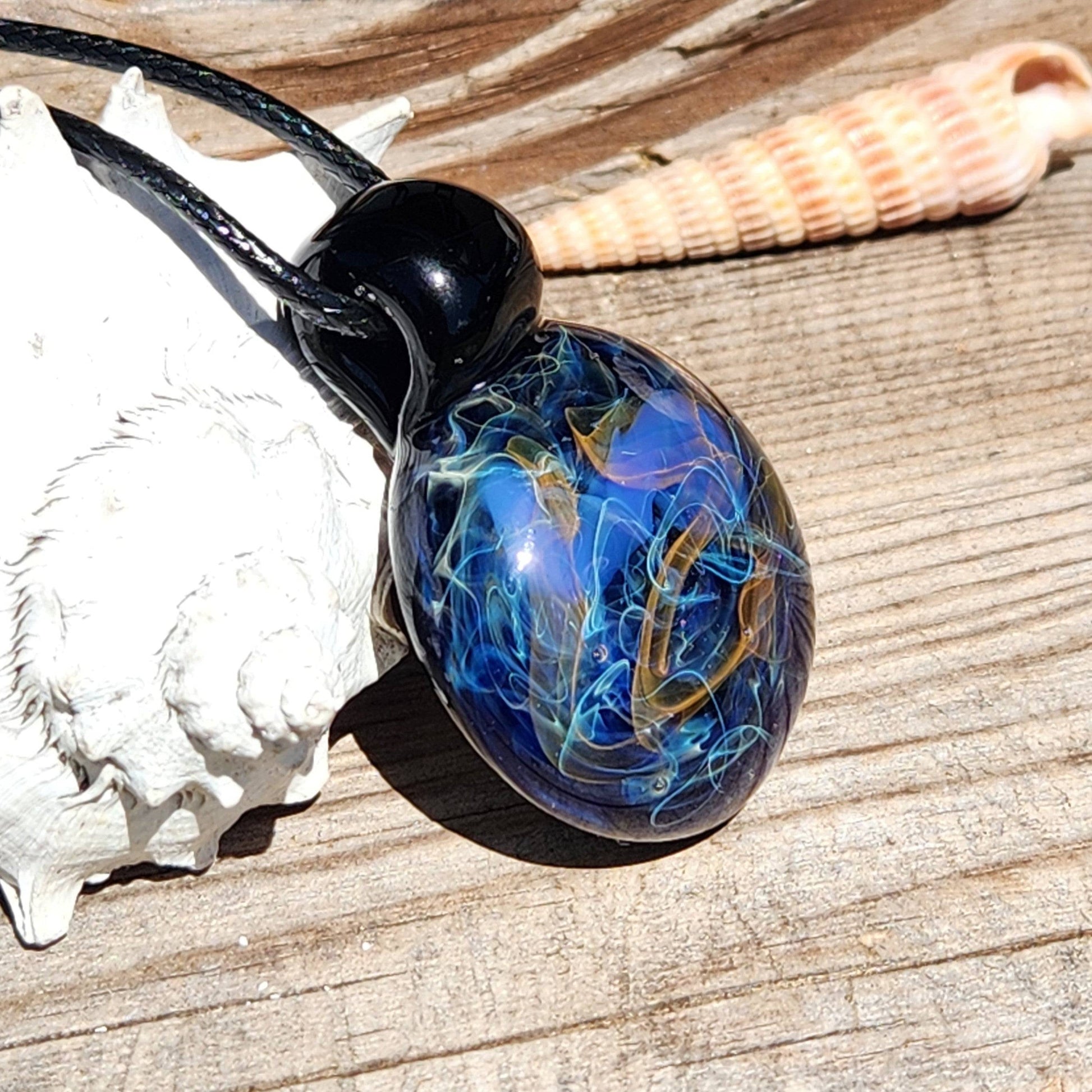Handmade Glass Pendant – Unique Gold & Silver Fumed Black Necklace displayed on wood with seashells, highlighting artistry.