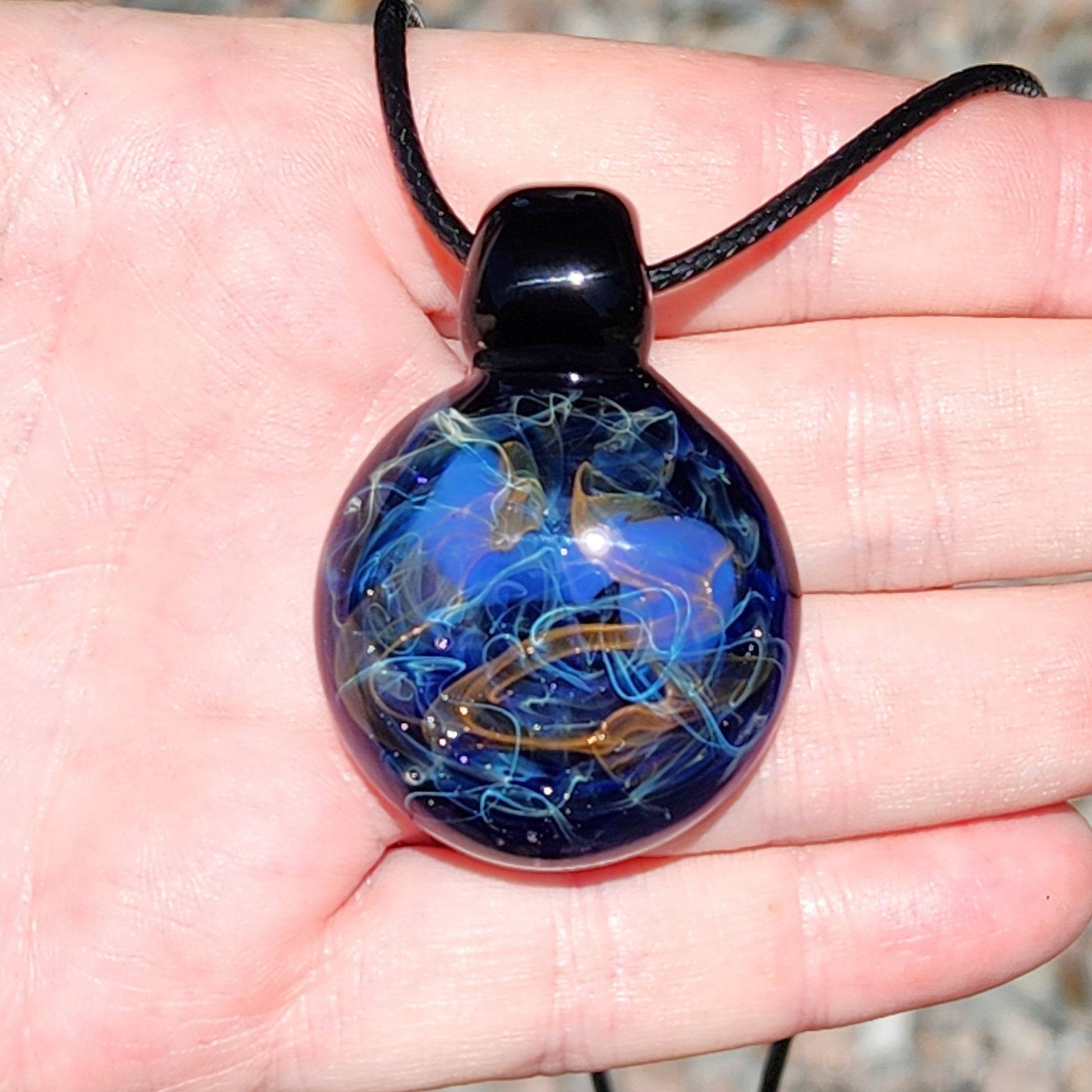 Front view of Handmade Glass Pendant – Unique Gold & Silver Fumed Black Necklace held in hand, showcasing galaxy swirl.