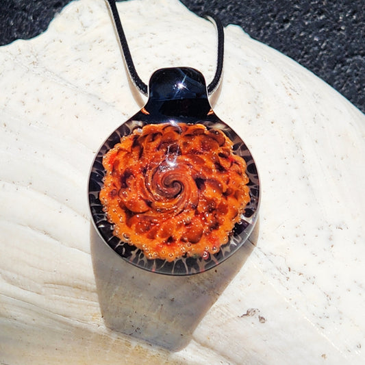 Bold spiral handmade glass pendant necklace in orange and black displayed on a white seashell, perfect for boho jewelry lovers.