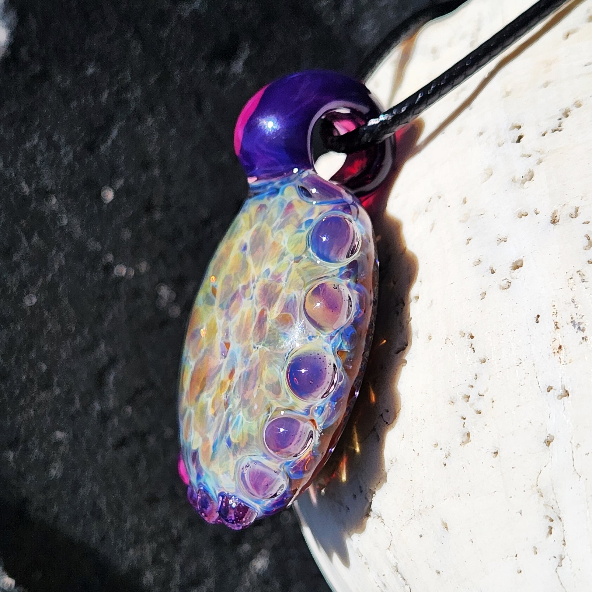 Side view of handmade rainbow glass pendant with iridescent shimmer and purple bubble accents. Artistic borosilicate statement necklace gift.