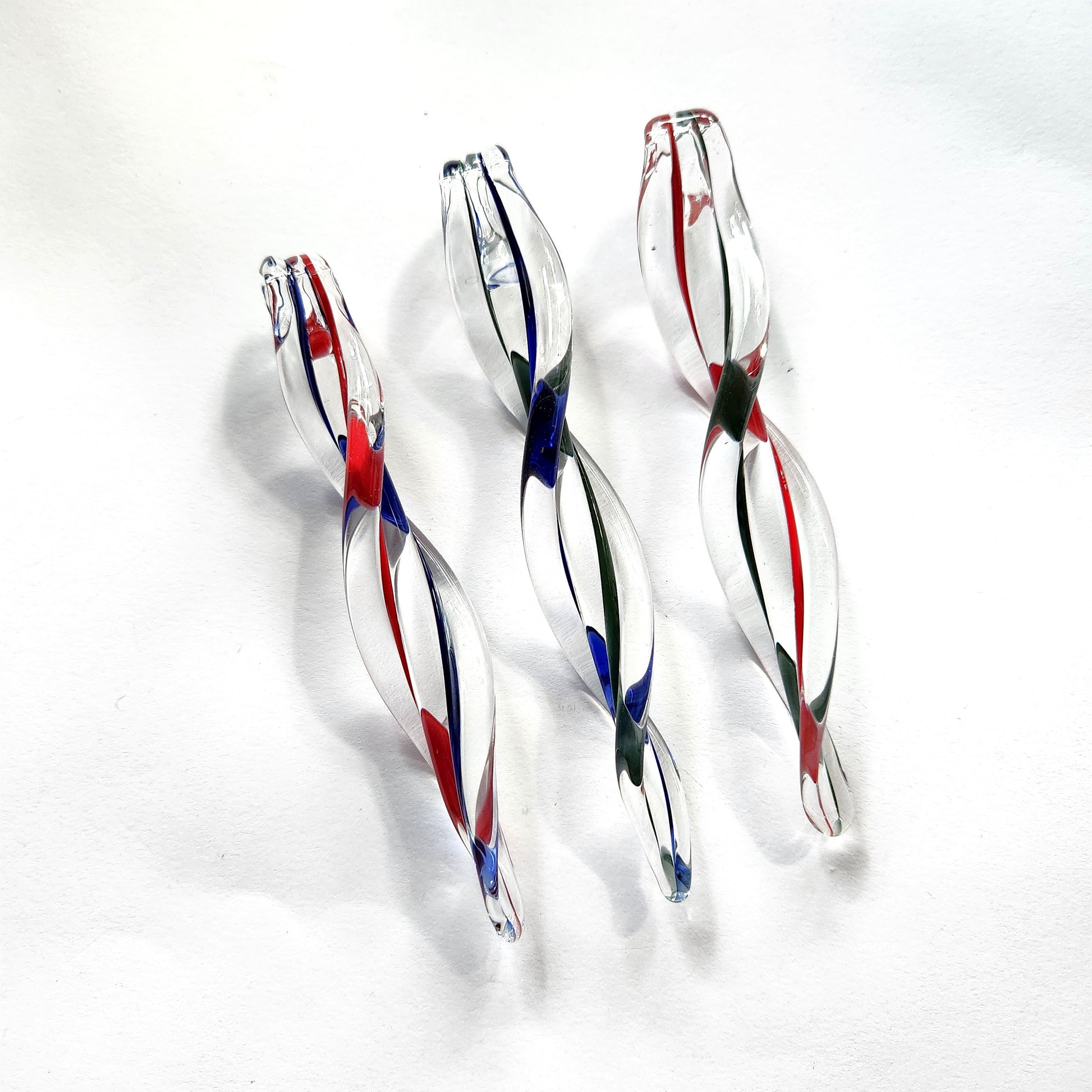 Three handblown glass icicle ornaments with red, green, and blue swirls on white background. Perfect for festive holiday decoration.
