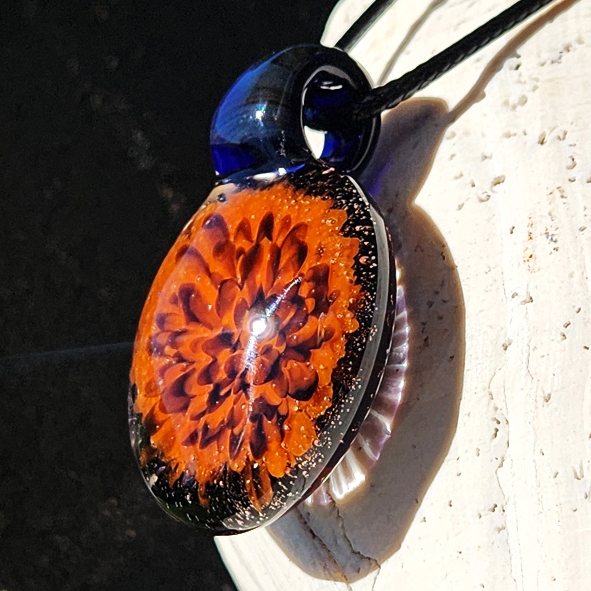 Handmade Fiery Flame Glass Pendant featuring a bold orange flower encased in clear glass with black accents. Fall-themed blown glass necklace.
