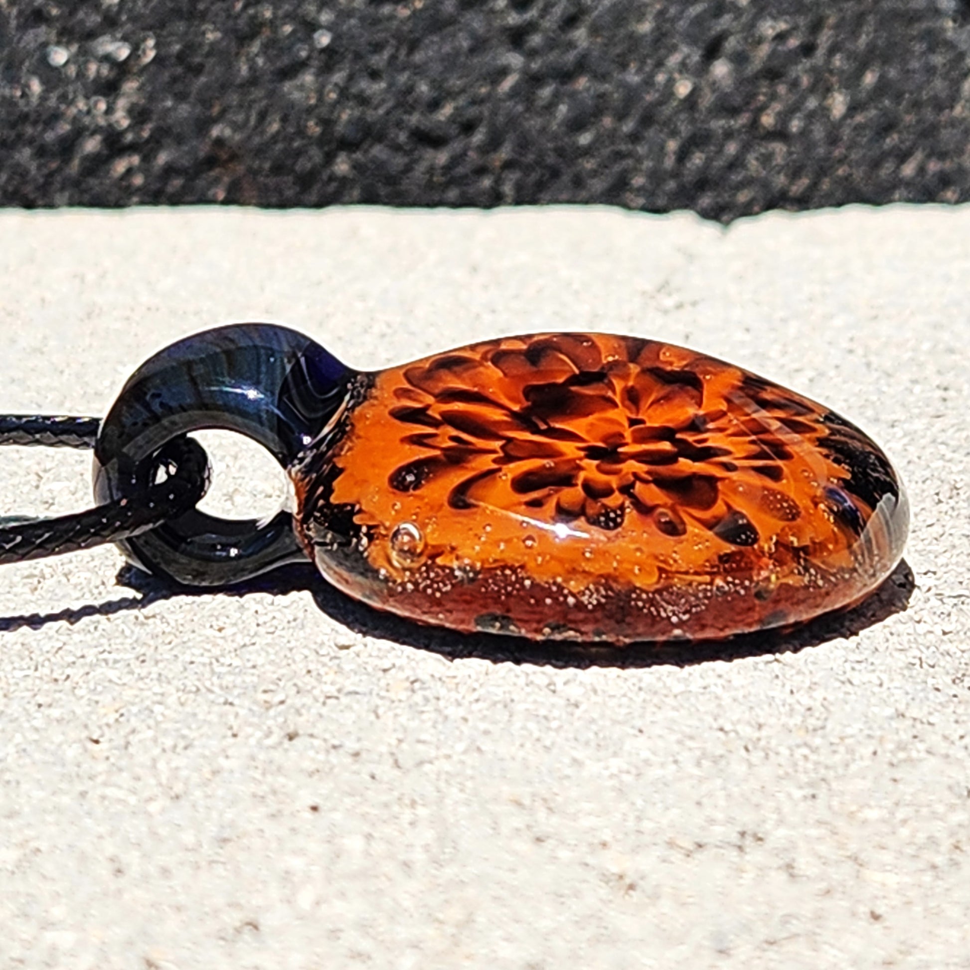 Close-up of Fiery Glass Pendant Necklace showing detailed red and orange bloom in blown glass. Handmade Halloween jewelry with black loop bail.