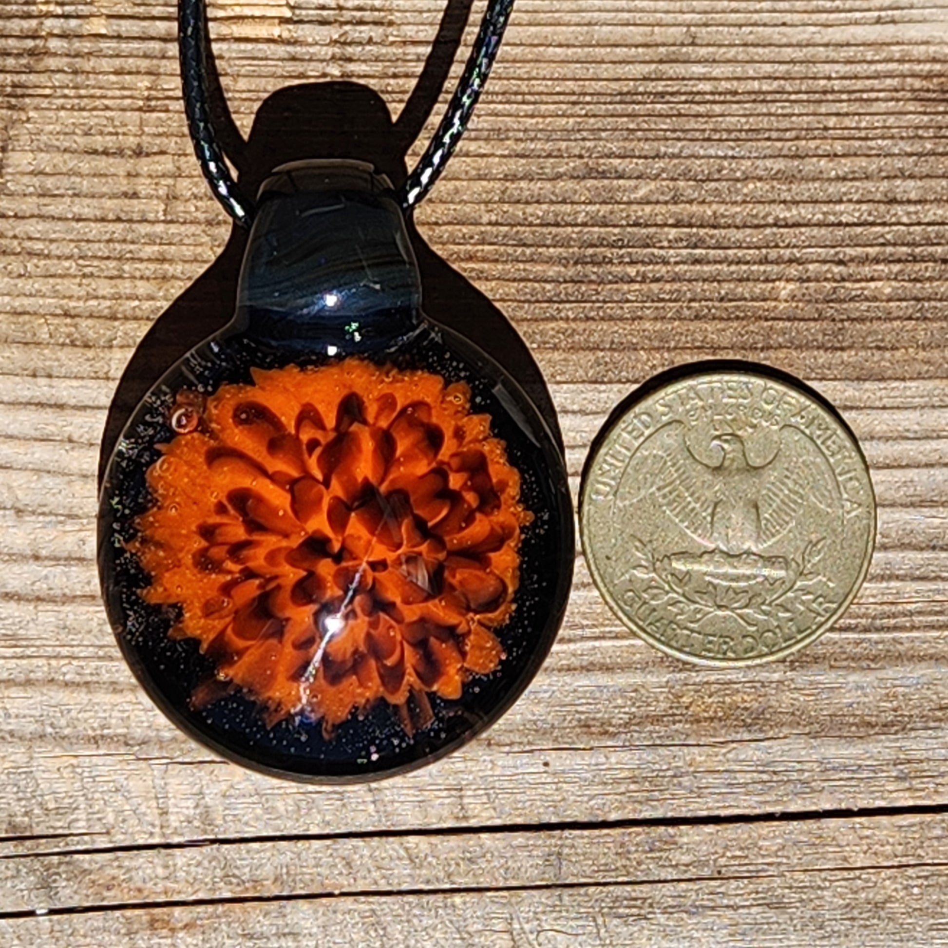 Fiery Glass Pendant Necklace next to a US quarter for size reference. Handmade blown glass jewelry with orange and red flame bloom.
