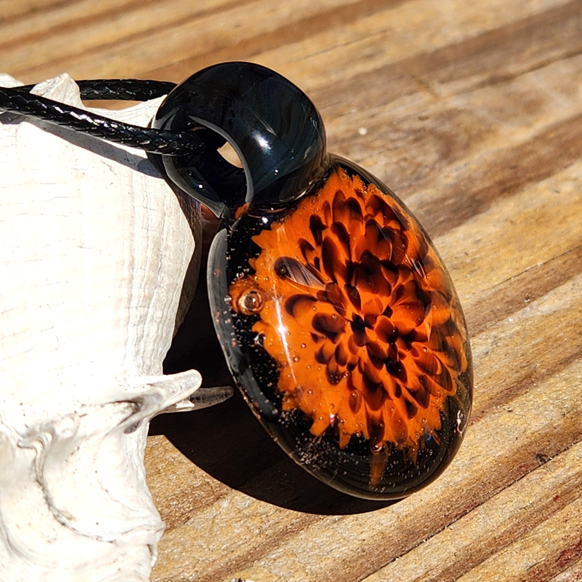 Angled view of Fiery Glass Pendant Necklace with glowing orange flower and black glass top. Handmade Halloween-inspired charm.