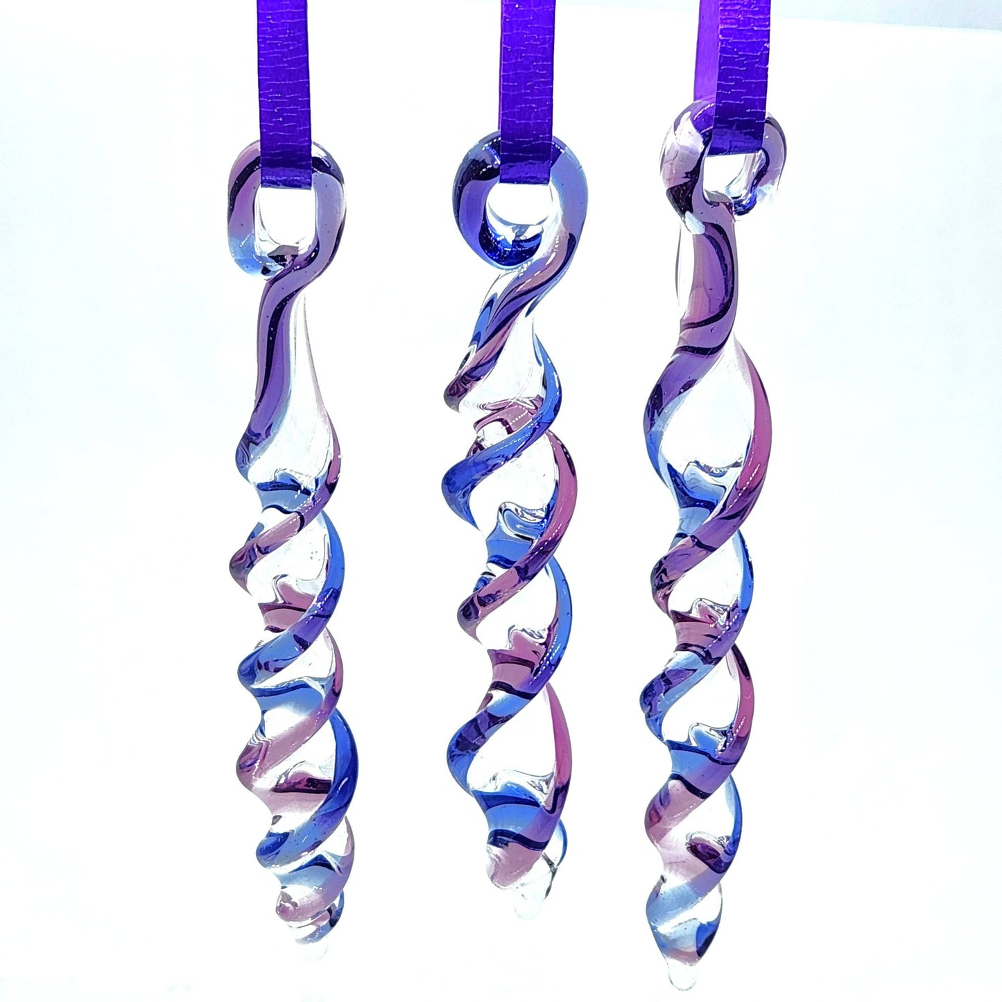 Trio of handmade blue and purple glass icicle ornaments hanging on purple ribbons, perfect as suncatchers or holiday decorations.