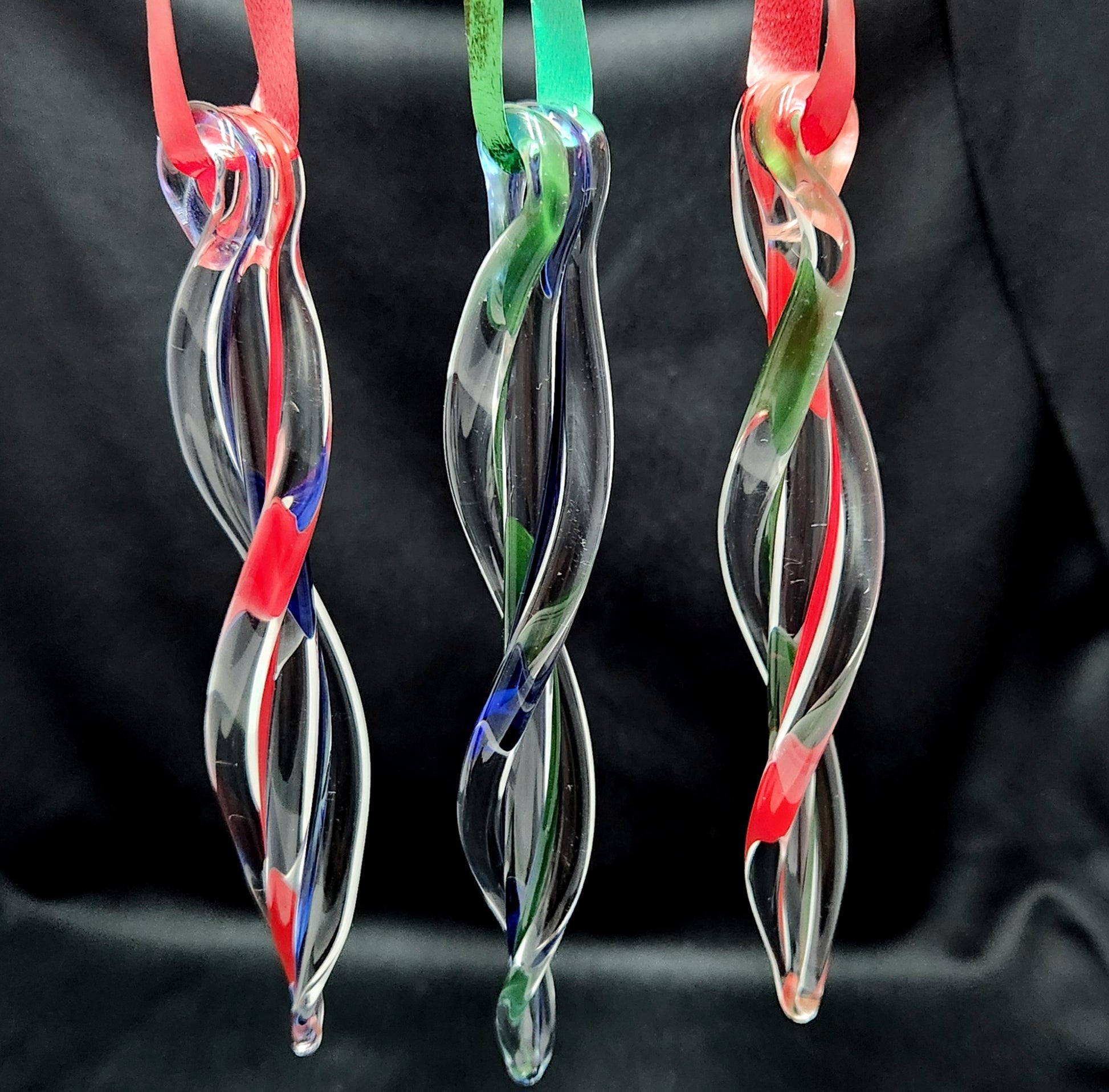 Three hanging handmade glass ornaments with red, green, and blue ribbons. Twisted icicle design adds sparkle to holiday decor.