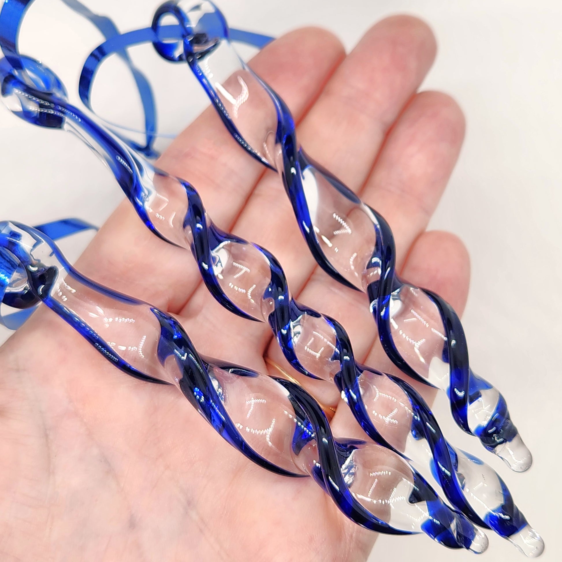 Hand holding three handmade blue glass Christmas icicle ornaments. Elegant suncatchers for festive tree or garden decoration.