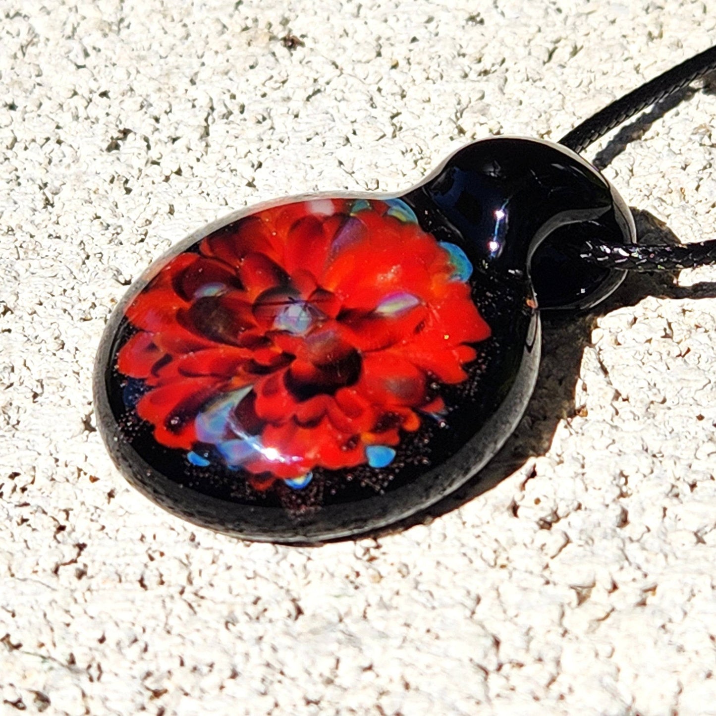 Flat-lay of radiant red glass pendant necklace on textured surface. Unique handmade borosilicate jewelry with bold red and blue accents.