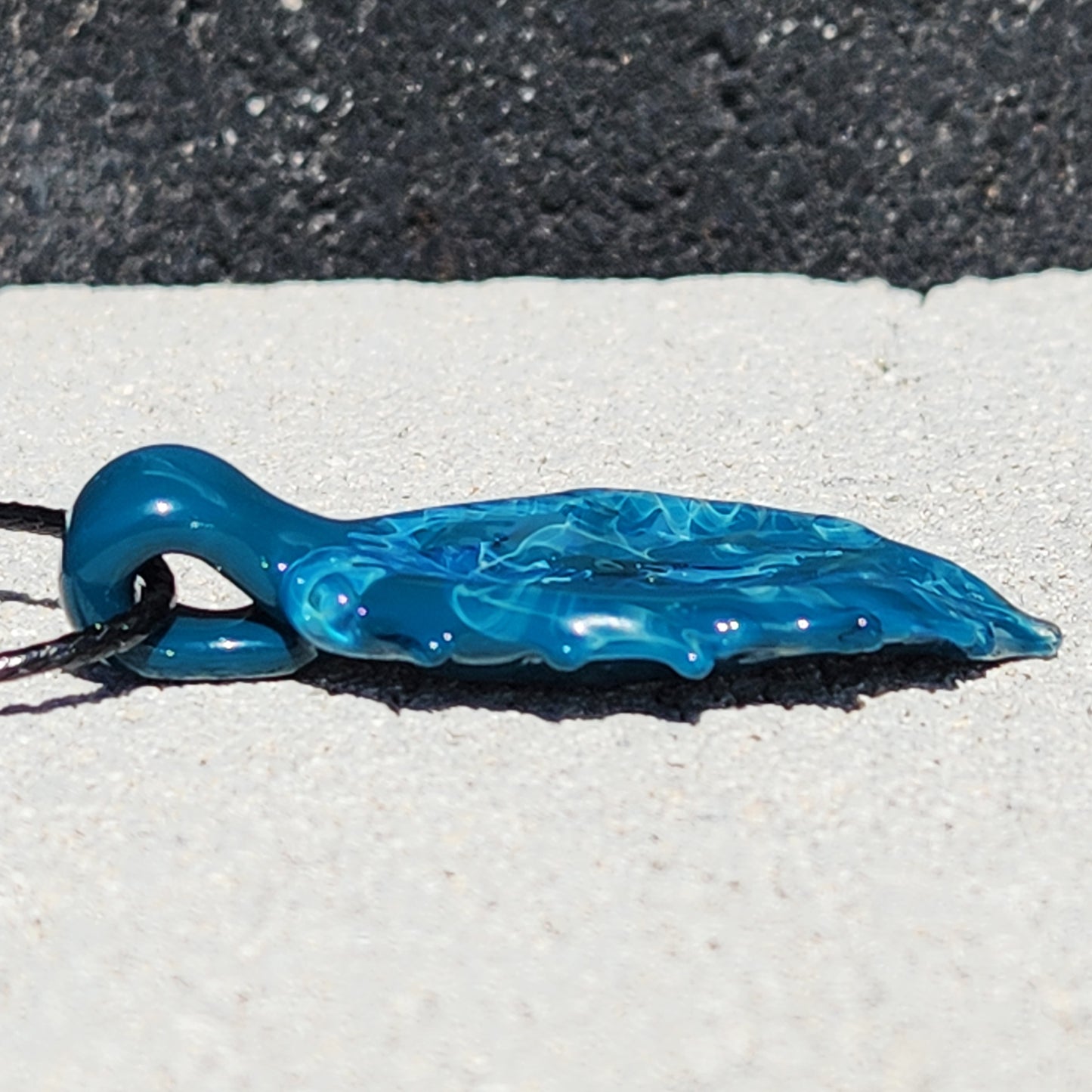 Flat side view of Ocean Drift Glass Pendant Necklace showing its lightweight, sculpted glass form in deep ocean blue tones.