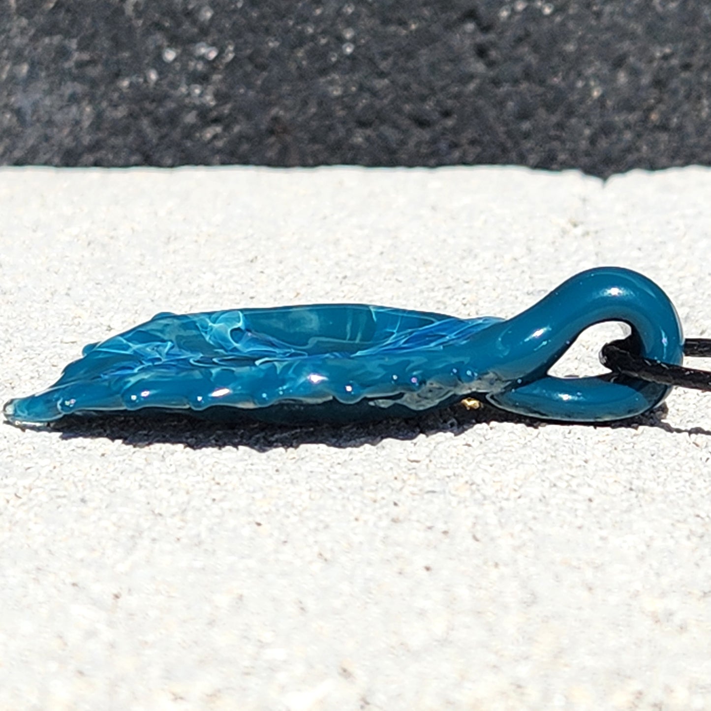 Low profile view of Ocean Drift Glass Pendant Necklace highlighting its smooth glass finish and unique wave-like texture.