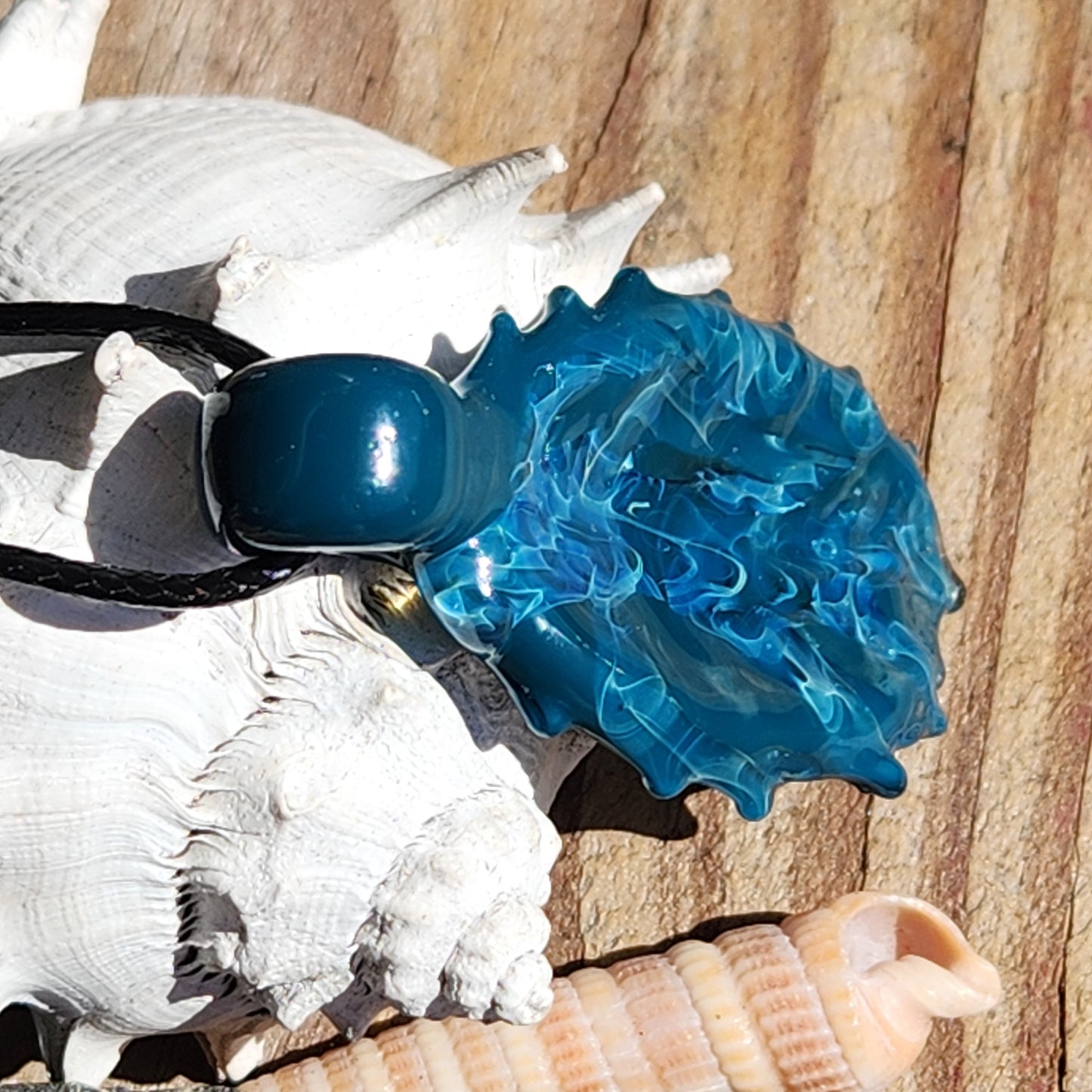 Ocean Drift Glass Pendant Necklace resting on seashells, highlighting its ocean wave texture and vibrant blue hues for coastal jewelry style.