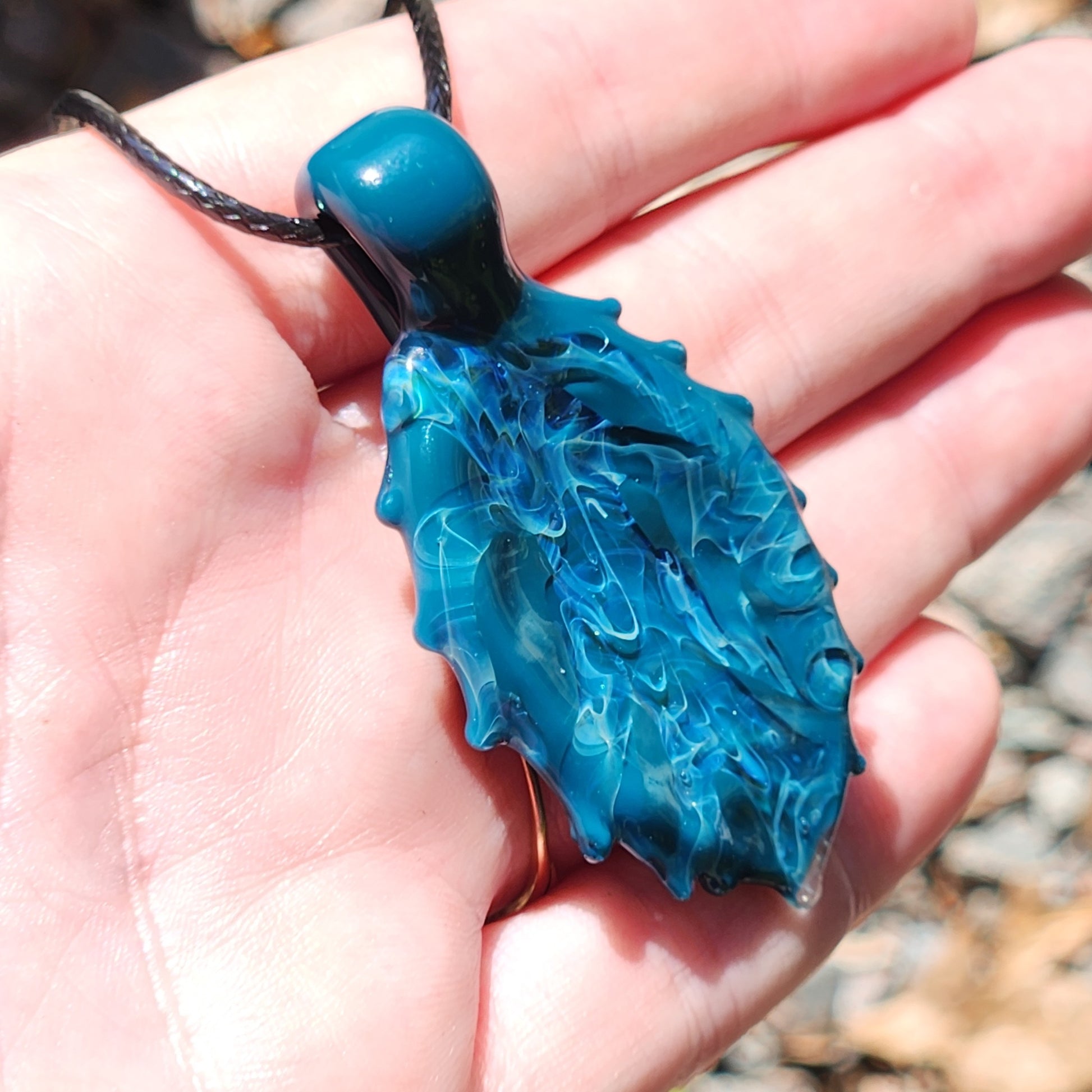 Ocean Drift Glass Pendant Necklace held in hand, displaying its textured ocean-inspired glass and lightweight craftsmanship.