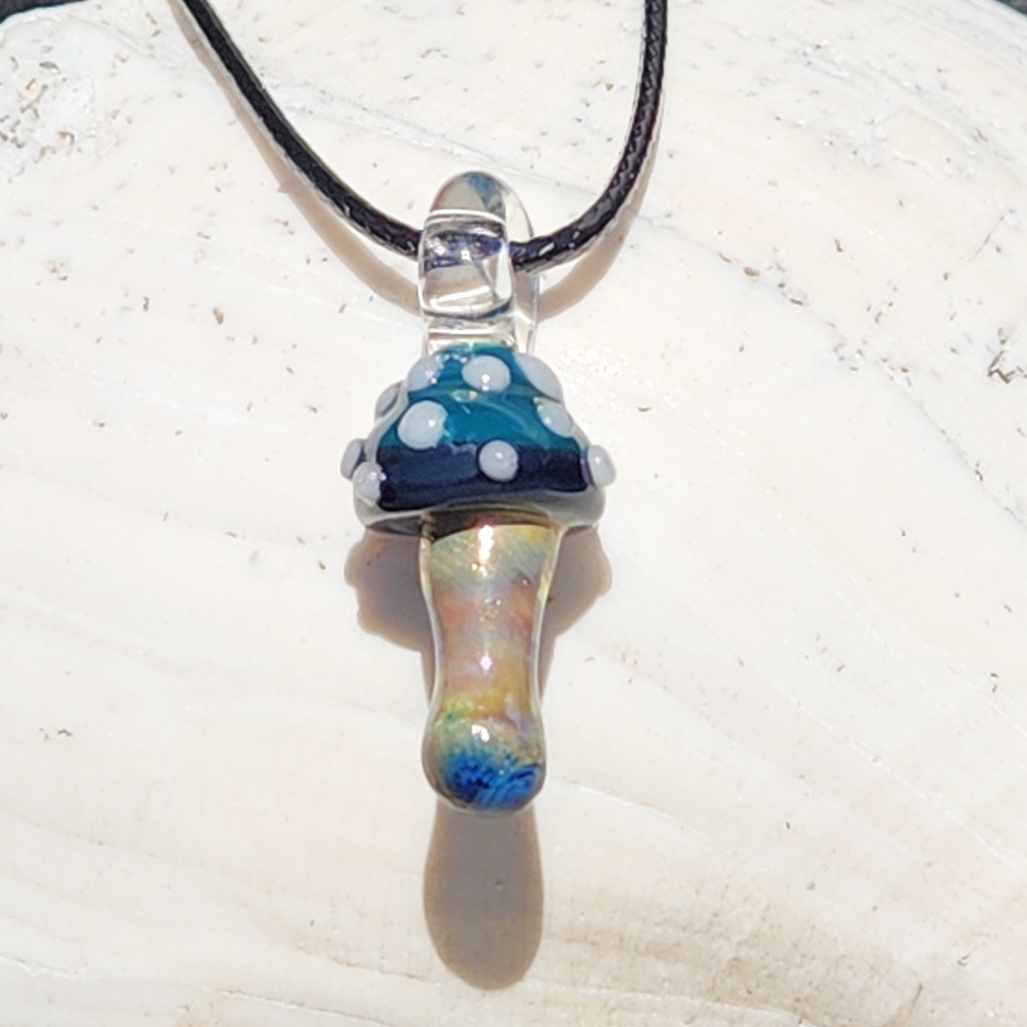 Blue Mushroom Art Glass Pendant with metallic stem and white polka dots on a black cord. Handmade mushroom necklace for boho jewelry lovers.